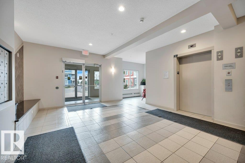 Building foyer featuring tile flooring, recessed lighting, double glass entry doors, and a passenger elevator - 219 1820 Rutherford Road, Edmonton, AB