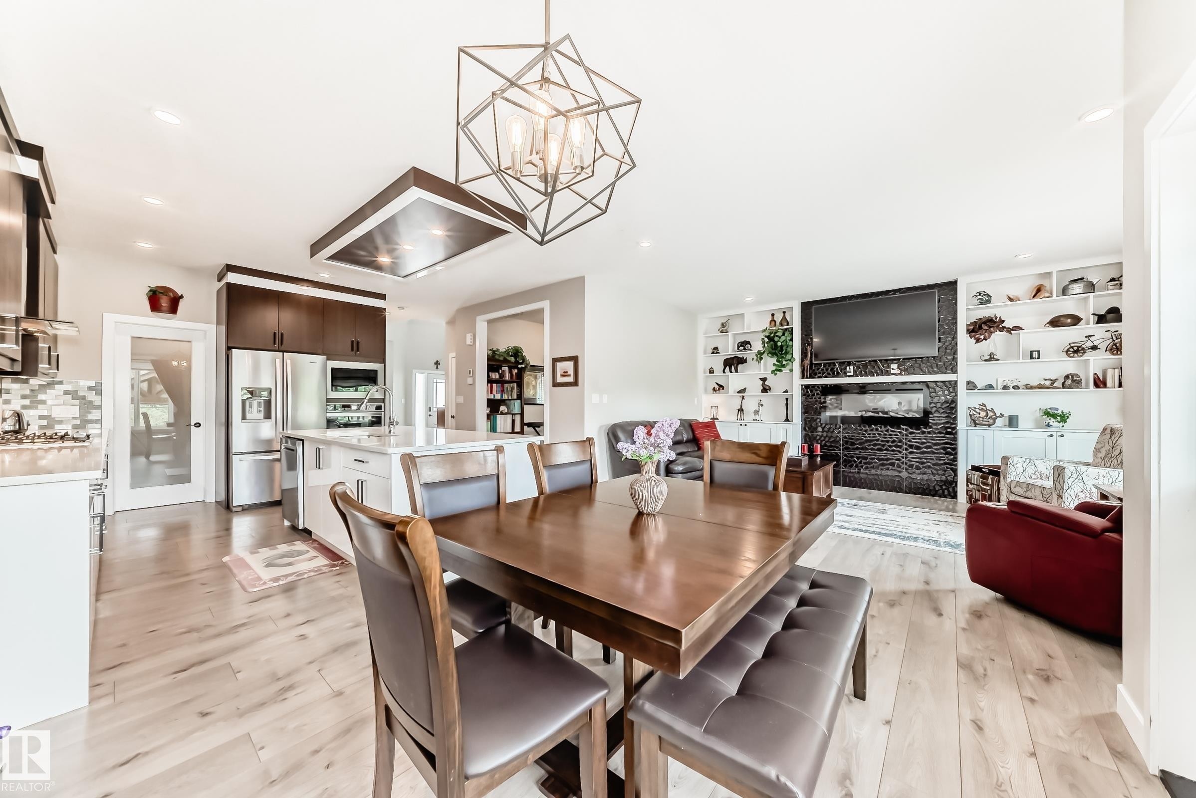 Open-concept living space with wood-finish flooring, a contemporary geometric chandelier, and built-in shelving surrounding a linear fireplace - 3895 Robins Crescent Nw, Edmonton, AB - Indoor Photo Showing Dining Room