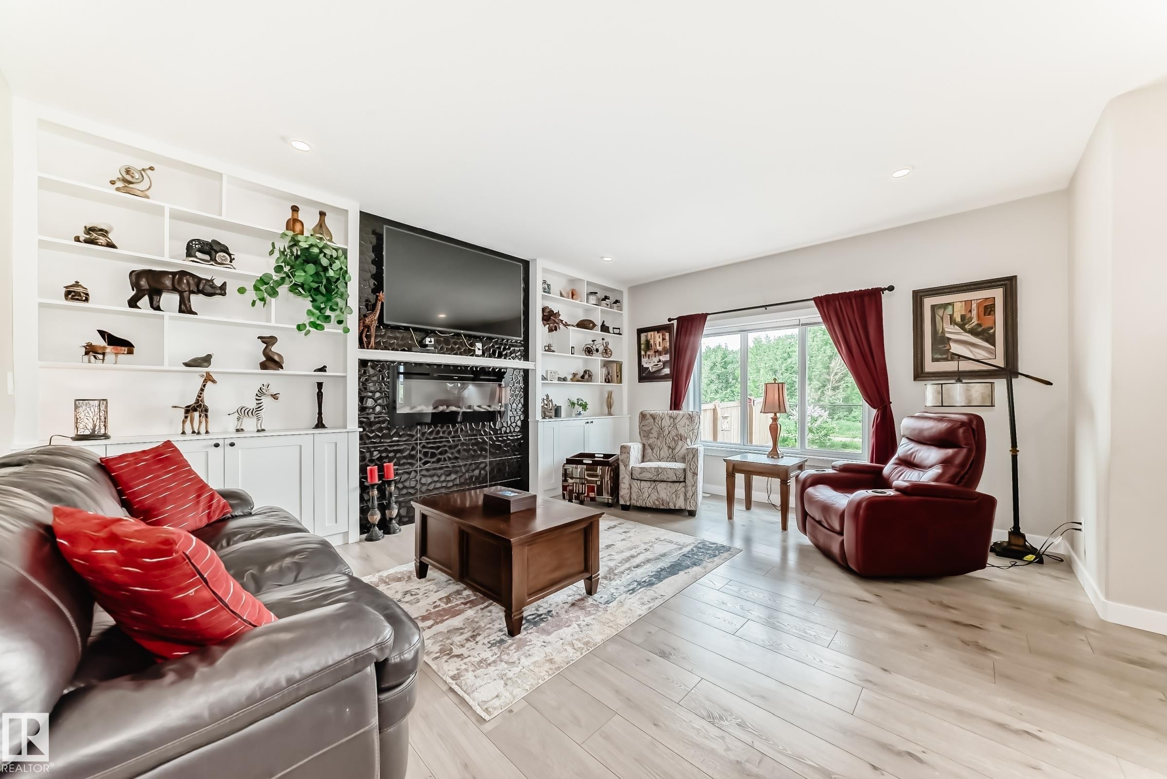 Living area featuring light wood-finish flooring, recessed lighting, and a prominent fireplace with a dark, textured surround - 3895 Robins Crescent Nw, Edmonton, AB - Indoor Photo Showing Living Room