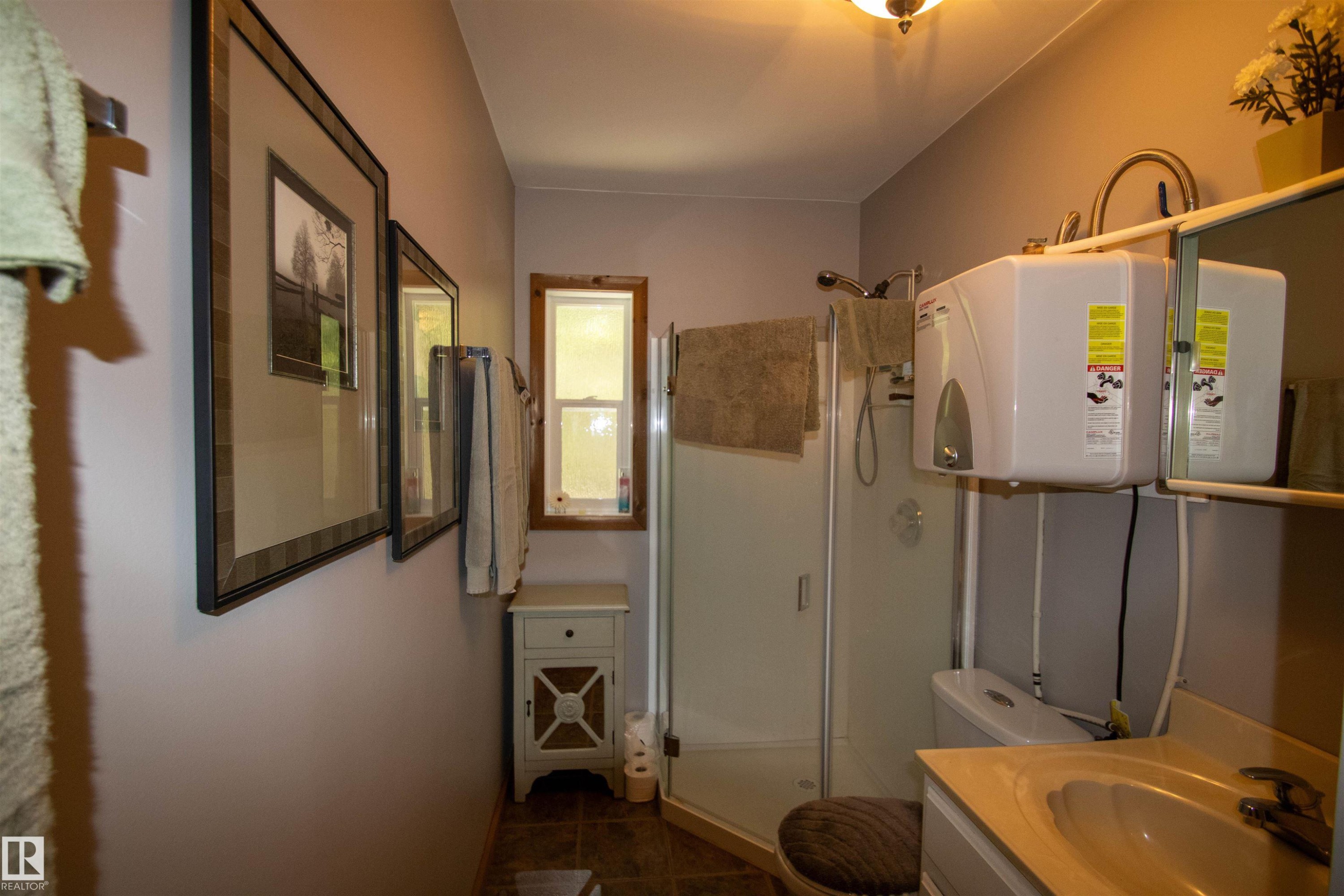 Bathroom featuring a glass-enclosed shower, single vanity with integrated sink, and wall-mounted water heater - 104 60201 Rng Rd 122, Rural St. Paul County, AB