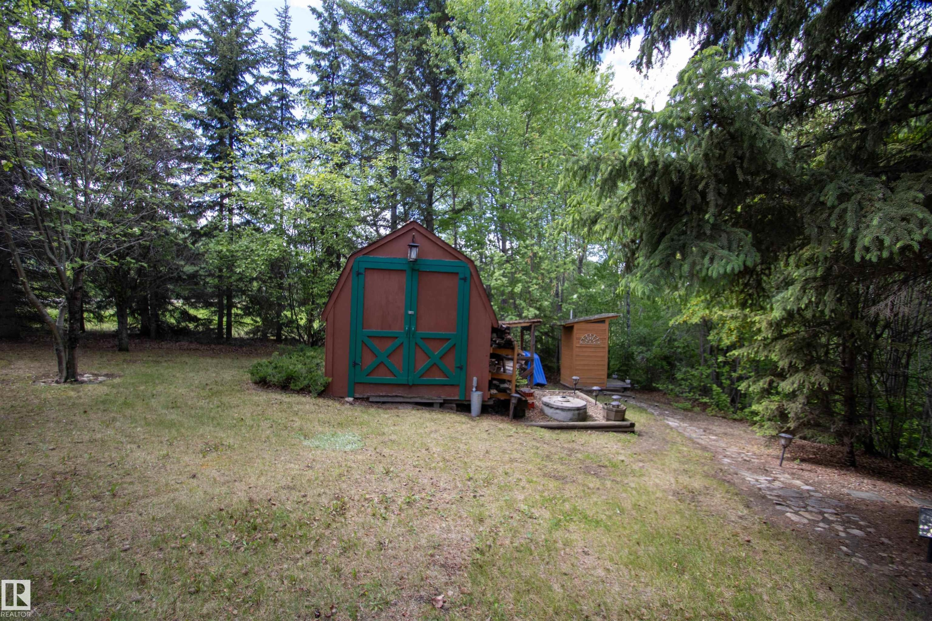 Expansive treed lot featuring a red and green storage shed, gravel pathway, and additional smaller shed - 104 60201 Rng Rd 122, Rural St. Paul County, AB