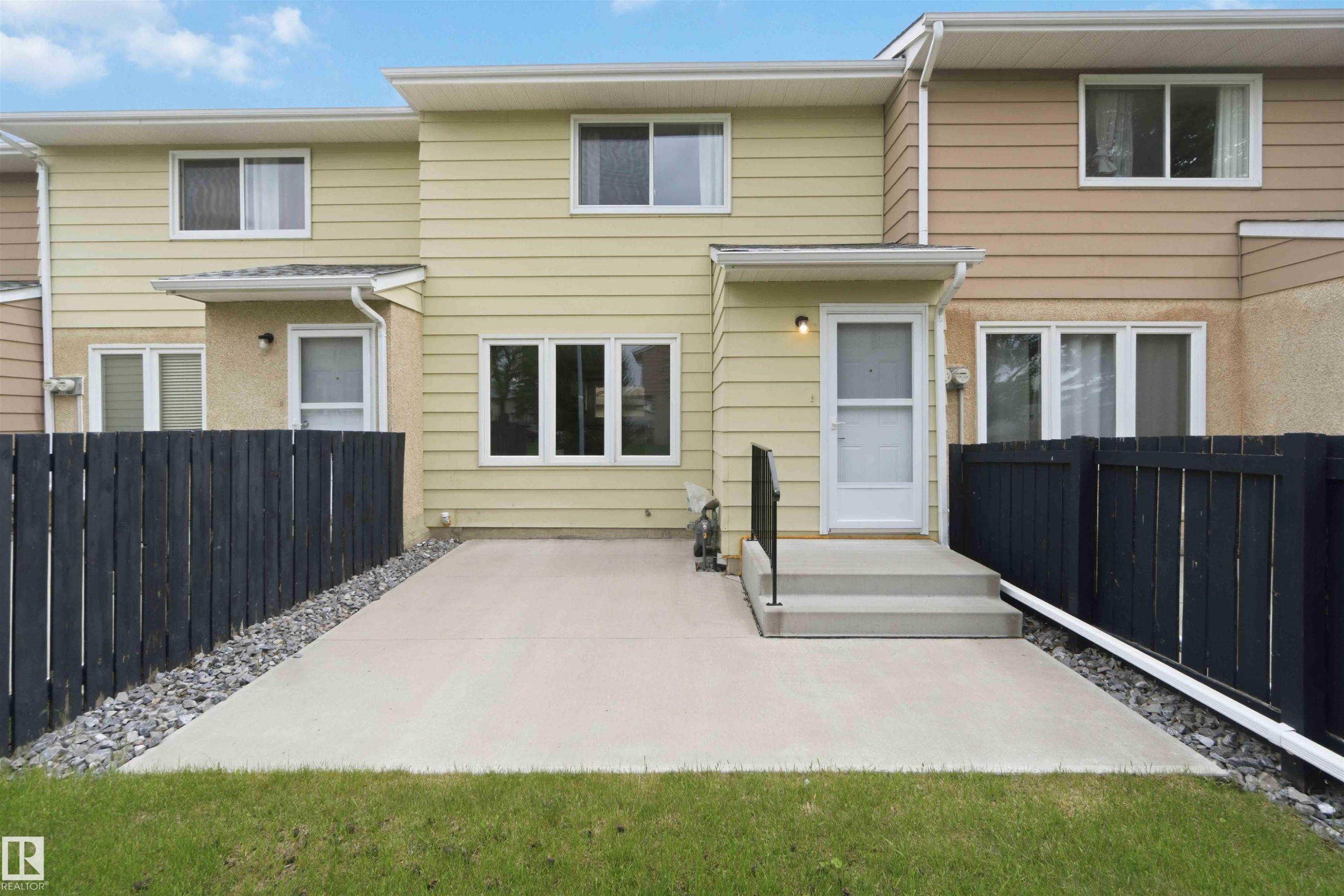 Rear exterior featuring a concrete patio, black wood fence, and a grass lawn - 17325 85 Avenue Nw, Edmonton, AB