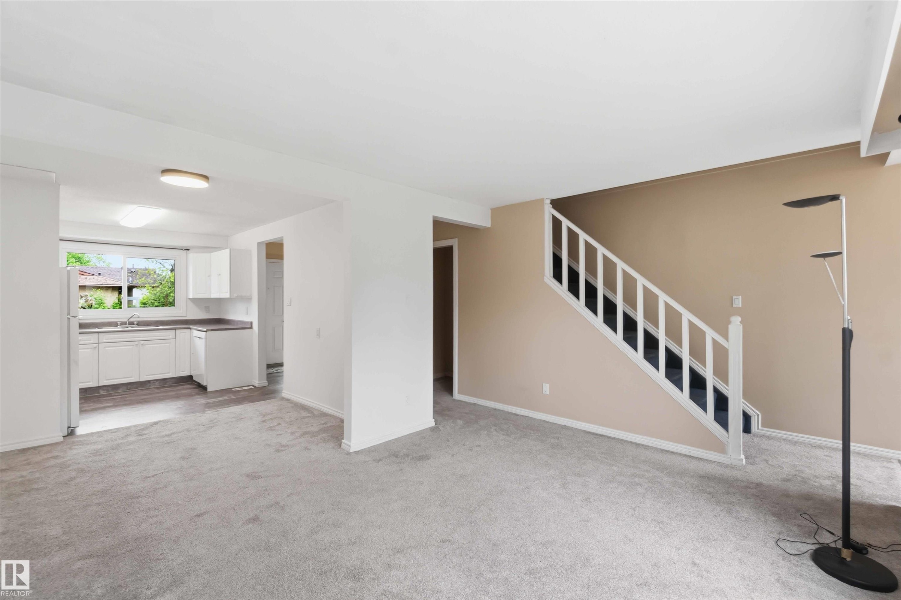 Open-concept living area featuring light gray carpeting and a white staircase with dark treads - 17325 85 Avenue Nw, Edmonton, AB