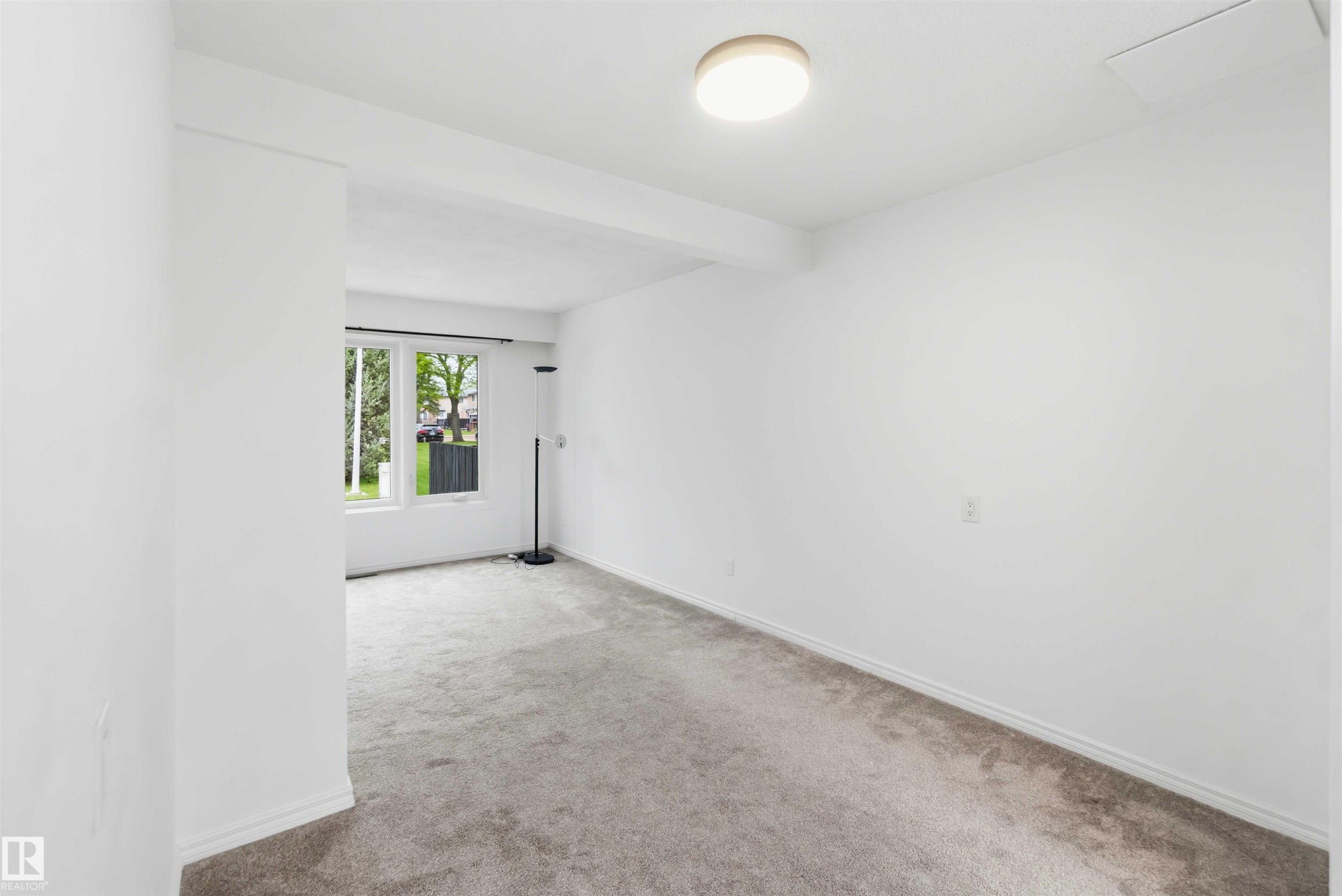 Bright interior room with white walls, grey carpet flooring, and a flush-mount ceiling light fixture - 17325 85 Avenue Nw, Edmonton, AB