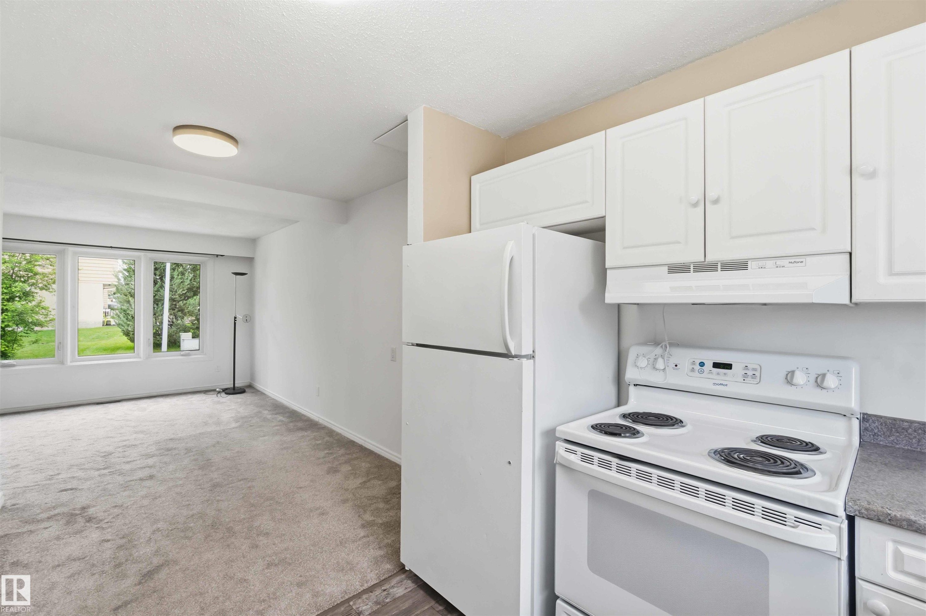 Kitchenette area featuring white cabinetry, a white refrigerator, and an electric range with an overhead exhaust fan - 17325 85 Avenue Nw, Edmonton, AB