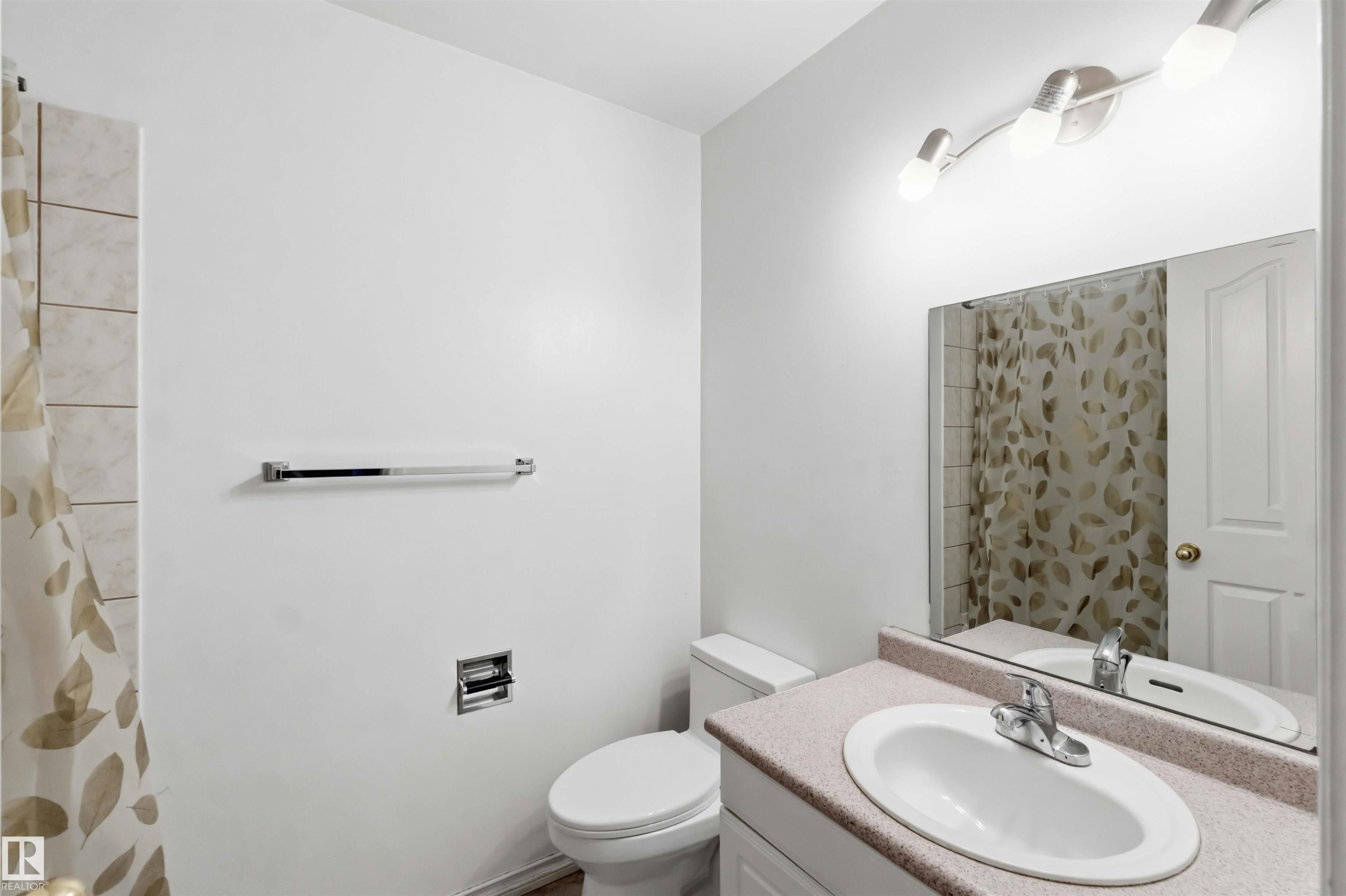 Bathroom featuring a white toilet, chrome towel bar, and a vanity with an integrated sink and laminate countertop - 17325 85 Avenue Nw, Edmonton, AB