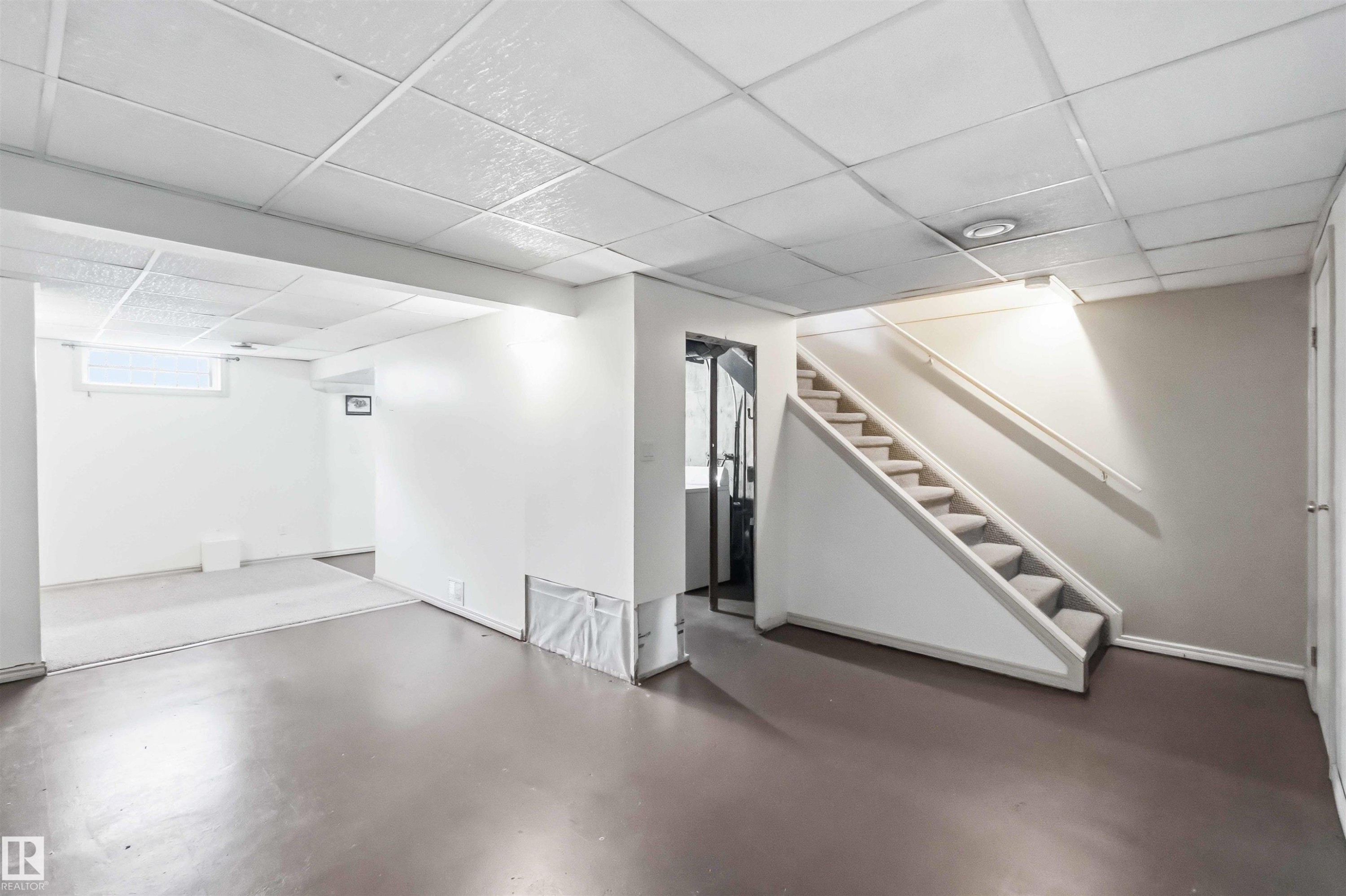 Finished lower level featuring a carpeted staircase with handrail, drop ceiling, and a distinct area with light-colored flooring - 17325 85 Avenue Nw, Edmonton, AB