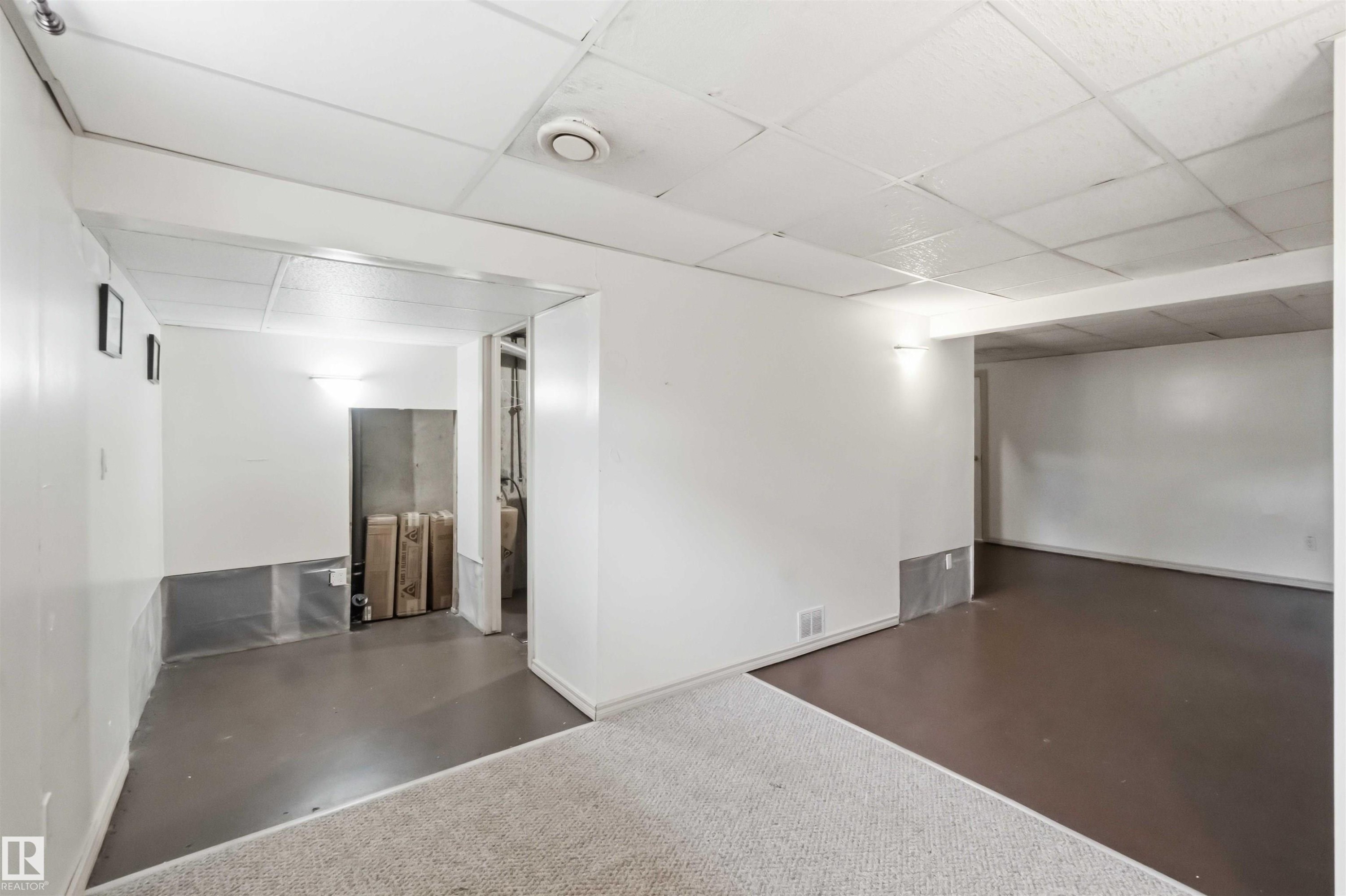 Versatile lower level featuring white walls, drop ceiling, and a combination of carpet and hard-surface flooring - 17325 85 Avenue Nw, Edmonton, AB