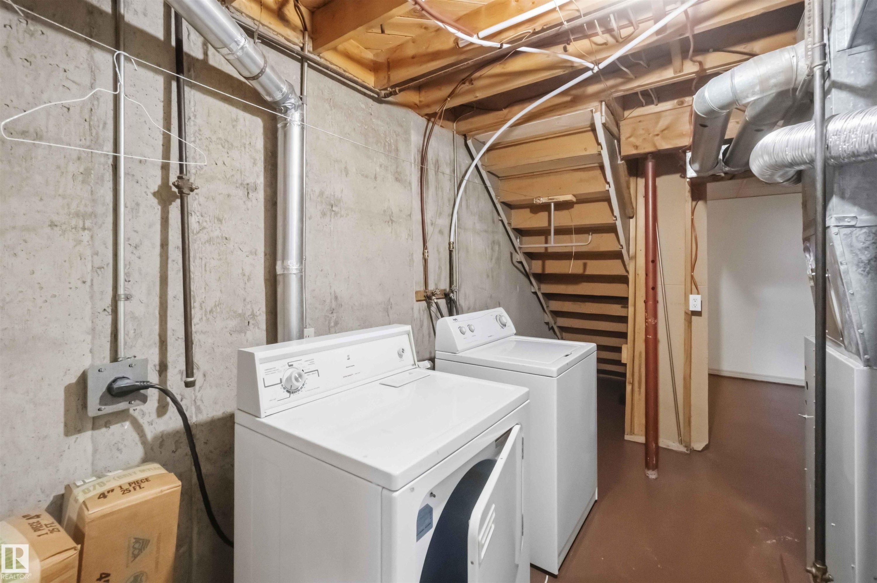 Utility space featuring a washer and dryer, exposed concrete walls, and wood-finish stairs - 17325 85 Avenue Nw, Edmonton, AB