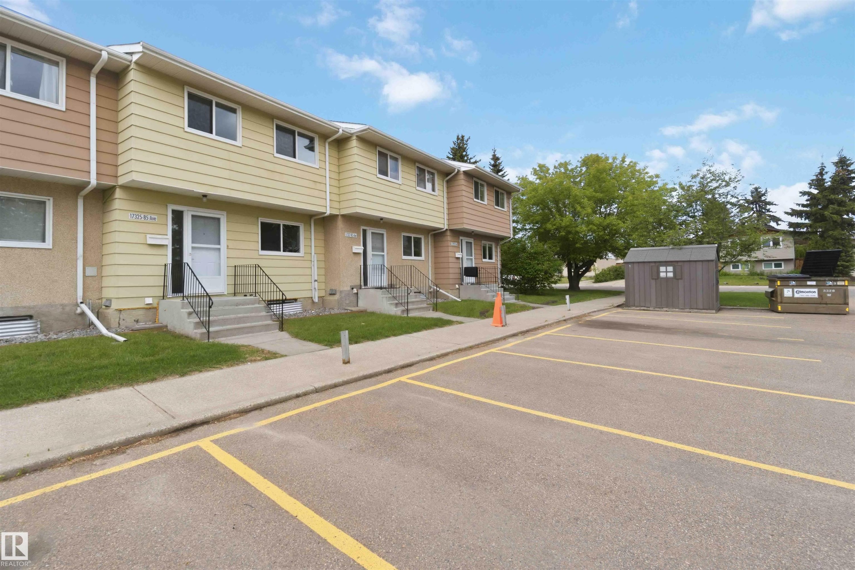 Townhouse exterior featuring a two-story design with siding and stucco finishes, individual front entrances with concrete steps and metal railings, and a manicured lawn - 17325 85 Avenue Nw, Edmonton, AB