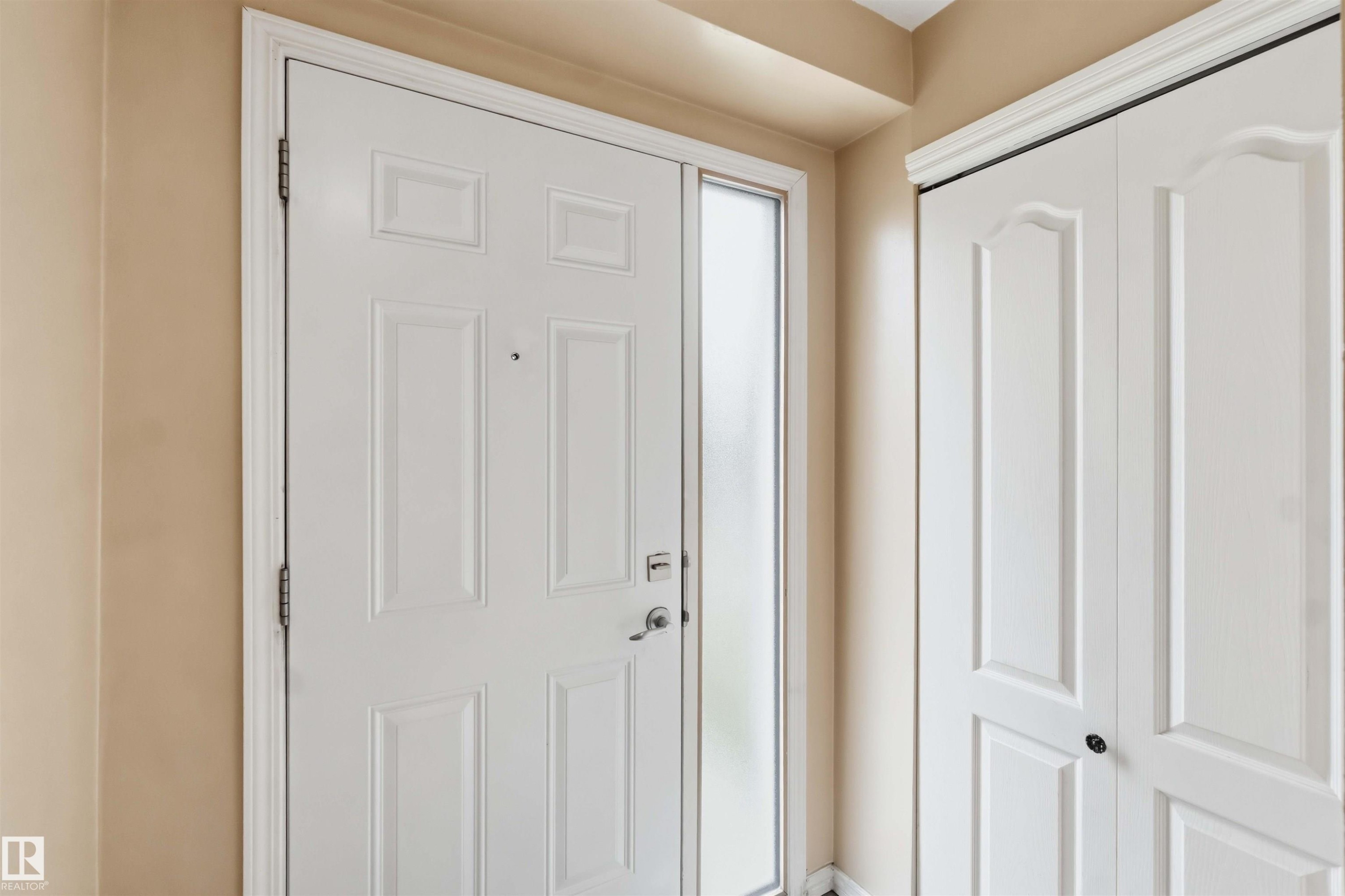 Entryway featuring a white paneled door with a sidelight, complementing the adjacent white bi-fold closet doors - 17325 85 Avenue Nw, Edmonton, AB