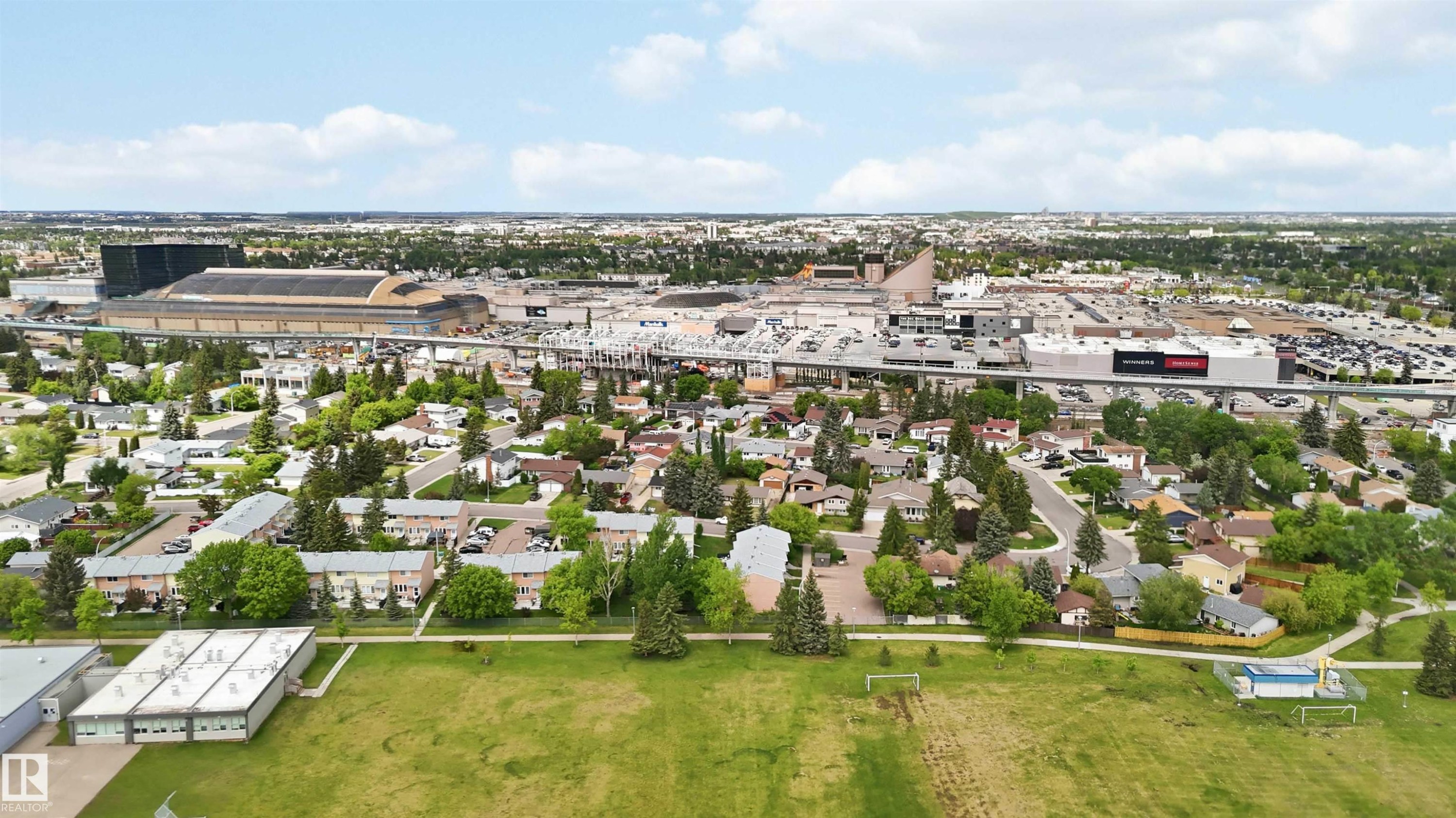 Expansive suburban landscape featuring residential homes and townhomes, mature trees, a large commercial complex, a transit line, and open green spaces - 17325 85 Avenue Nw, Edmonton, AB