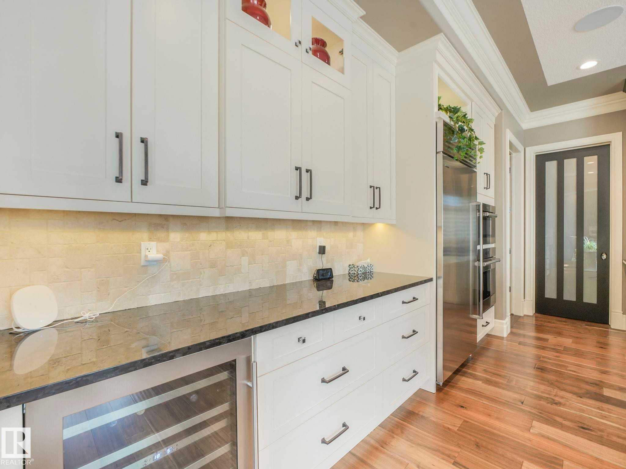 White shaker cabinetry with dark hardware, dark stone countertops, a tiled backsplash, and wood-finish flooring - 2807 Wheaton Drive, Edmonton, AB