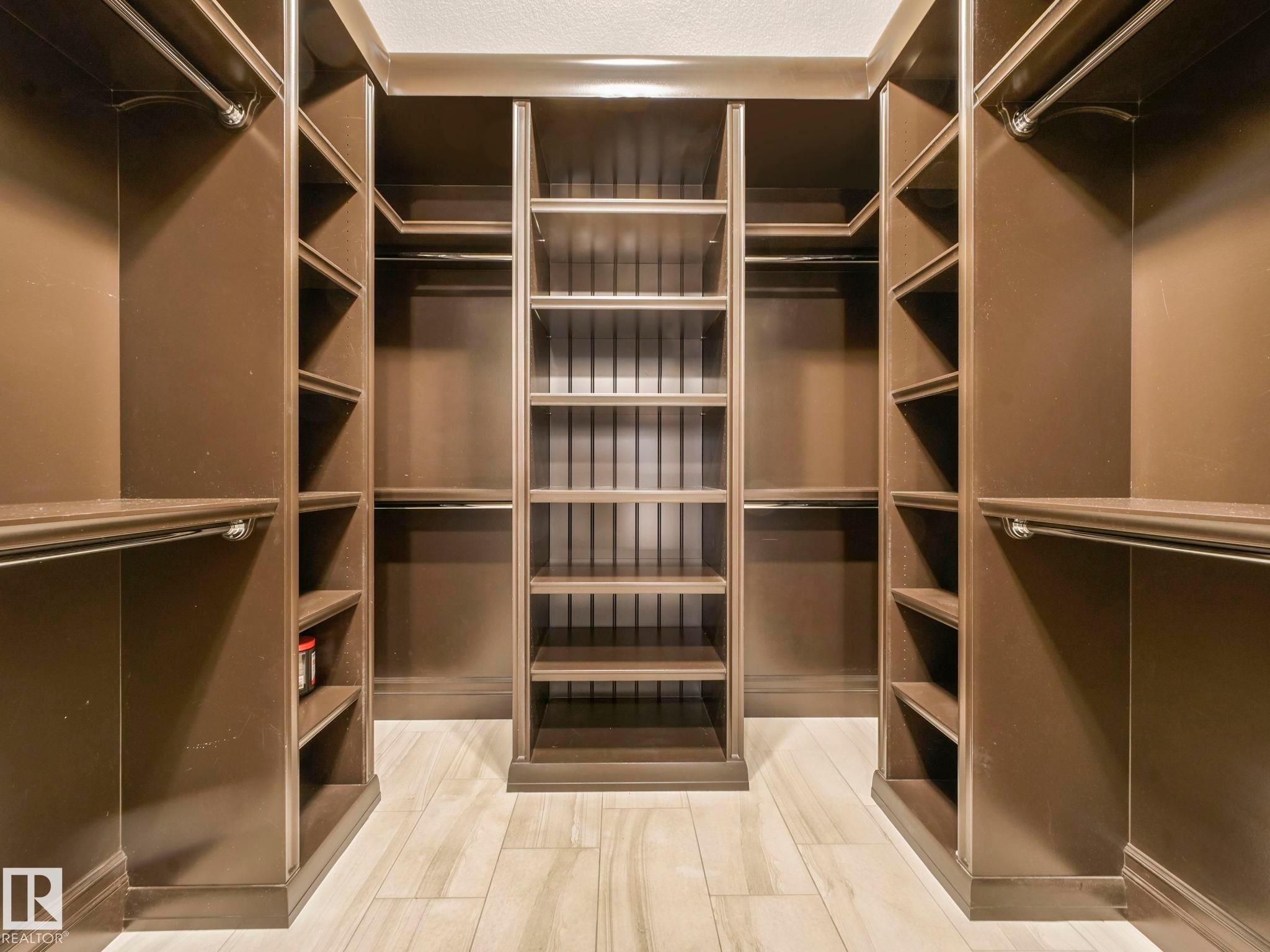 Custom closet system featuring dark wood-finish cabinetry, extensive shelving, multiple hanging rods, and wood-finish flooring - 2807 Wheaton Drive, Edmonton, AB