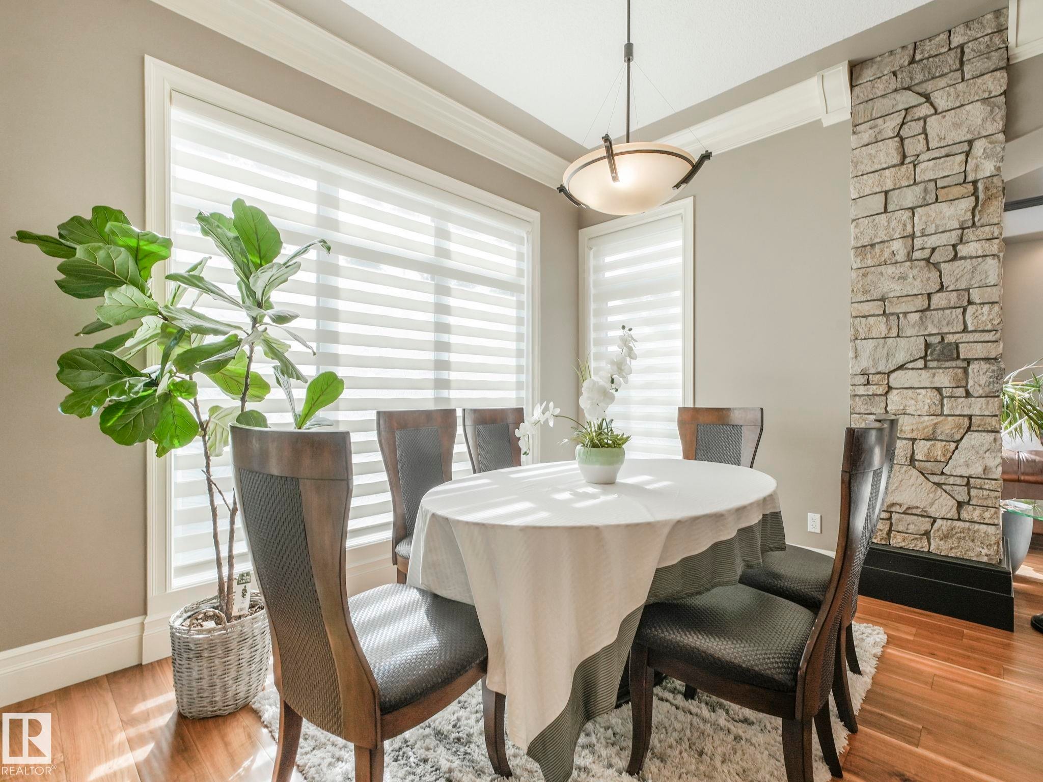 Dining area featuring wood-finish flooring, a stone-clad architectural column, and a tray ceiling with crown molding - 2807 Wheaton Drive, Edmonton, AB