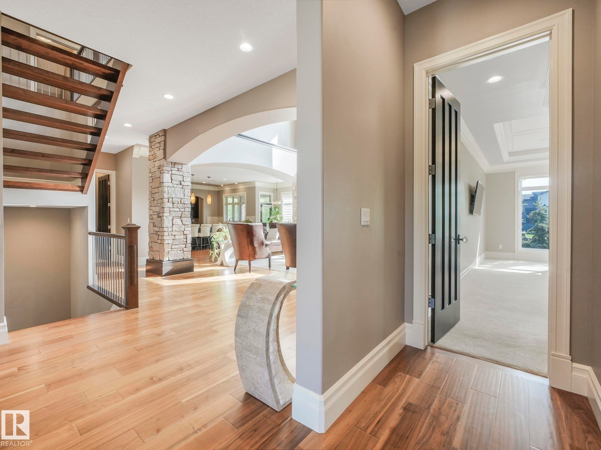 Spacious hallway featuring wood-finish flooring, a contemporary open-riser staircase with a wood and metal railing, and a stone-clad architectural column - 2807 Wheaton Drive, Edmonton, AB