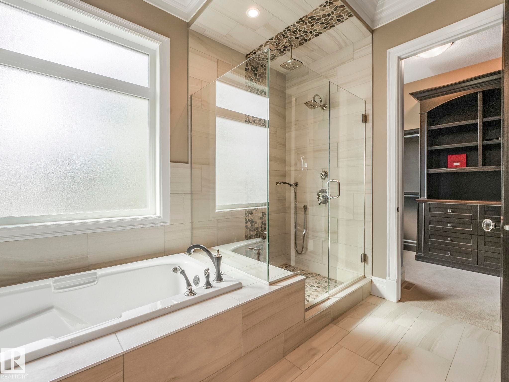Bathroom featuring a freestanding tub with deck-mounted fixtures, a glass-enclosed shower with a rainfall showerhead and pebble-tile floor, and large format wall and floor tiling - 2807 Wheaton Drive, Edmonton, AB