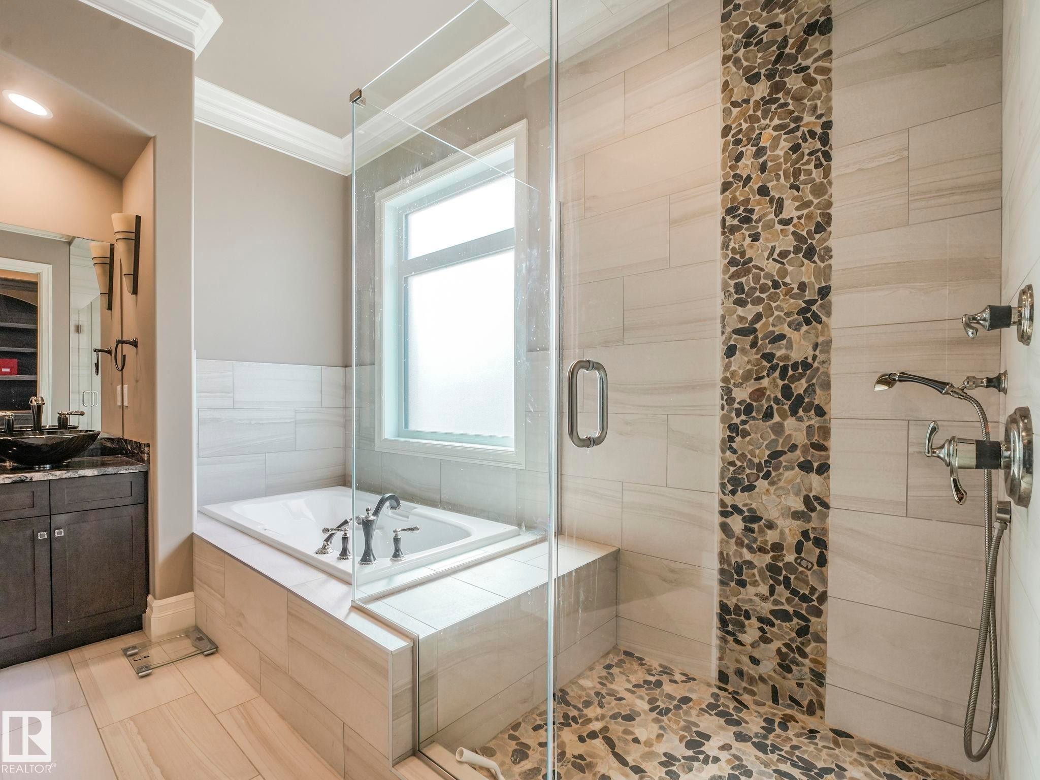 Oversized soaking tub with surrounding tile surround, frameless glass shower enclosure, and a natural stone pebble-tiled shower floor and accent wall - 2807 Wheaton Drive, Edmonton, AB