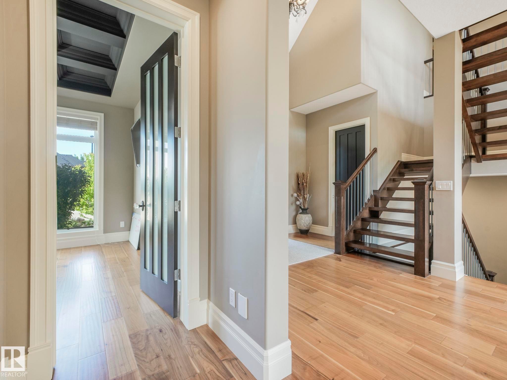 Entryway featuring wood-finish flooring, a contemporary dark wood staircase with black spindles, and a coffered ceiling in an adjacent room - 2807 Wheaton Drive, Edmonton, AB