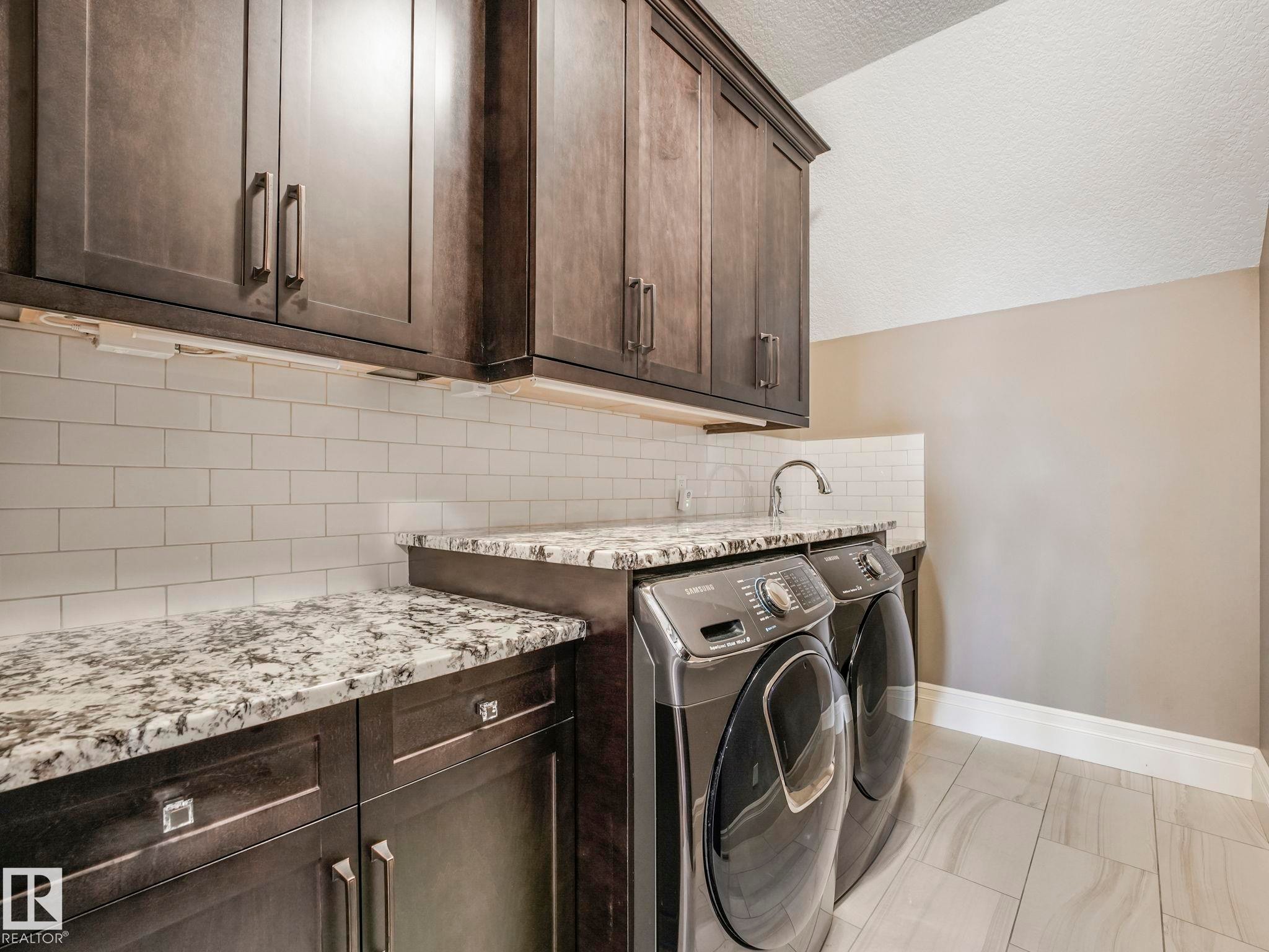 Utility area featuring dark wood-finish cabinetry, speckled countertops, a subway tile backsplash, and light-toned tile flooring - 2807 Wheaton Drive, Edmonton, AB