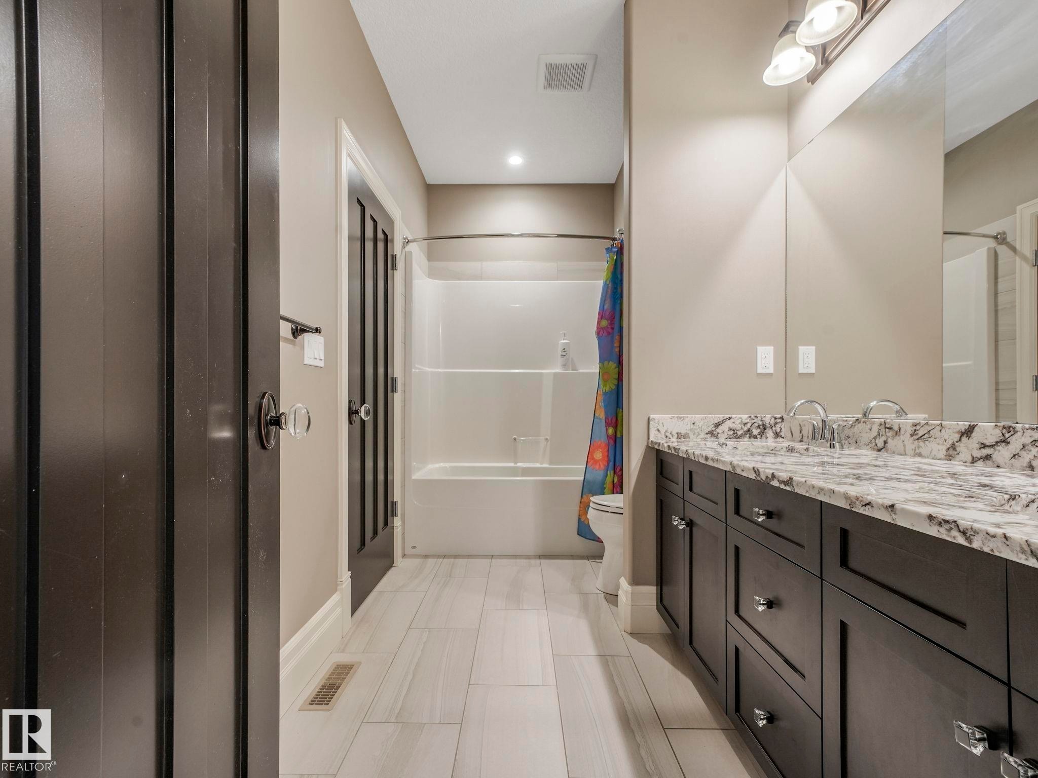 Spacious bathroom featuring a dual vanity with a patterned stone countertop, dark wood cabinetry, and a full-width mirror - 2807 Wheaton Drive, Edmonton, AB