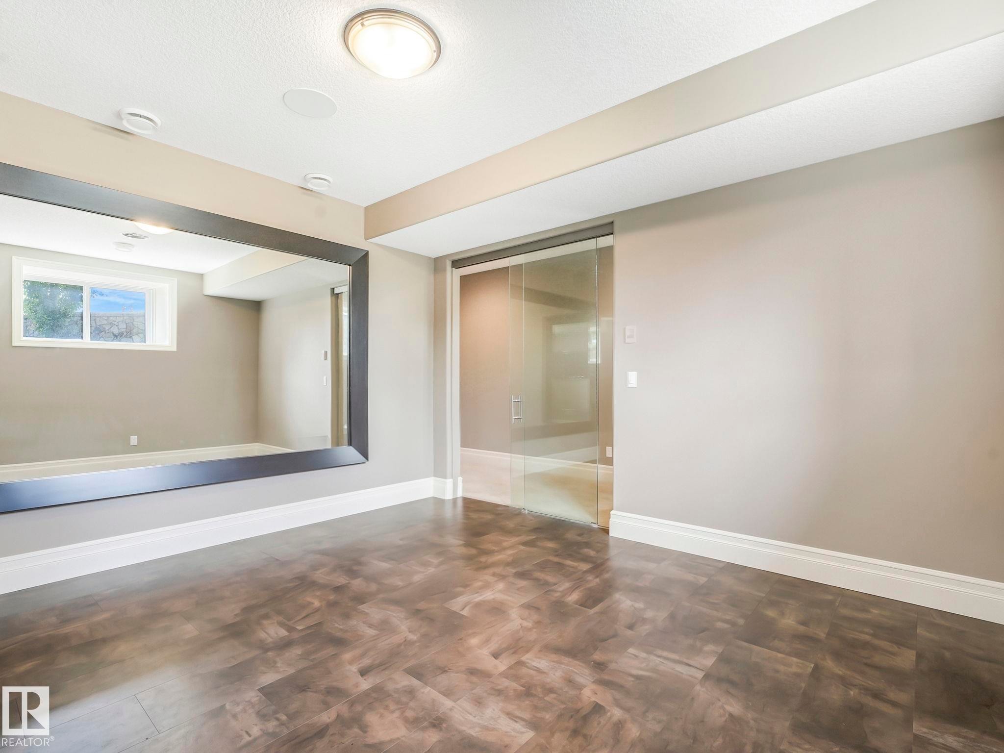 Spacious room featuring wood-finish flooring, a large wall-mounted mirror, and a glass sliding door - 2807 Wheaton Drive, Edmonton, AB