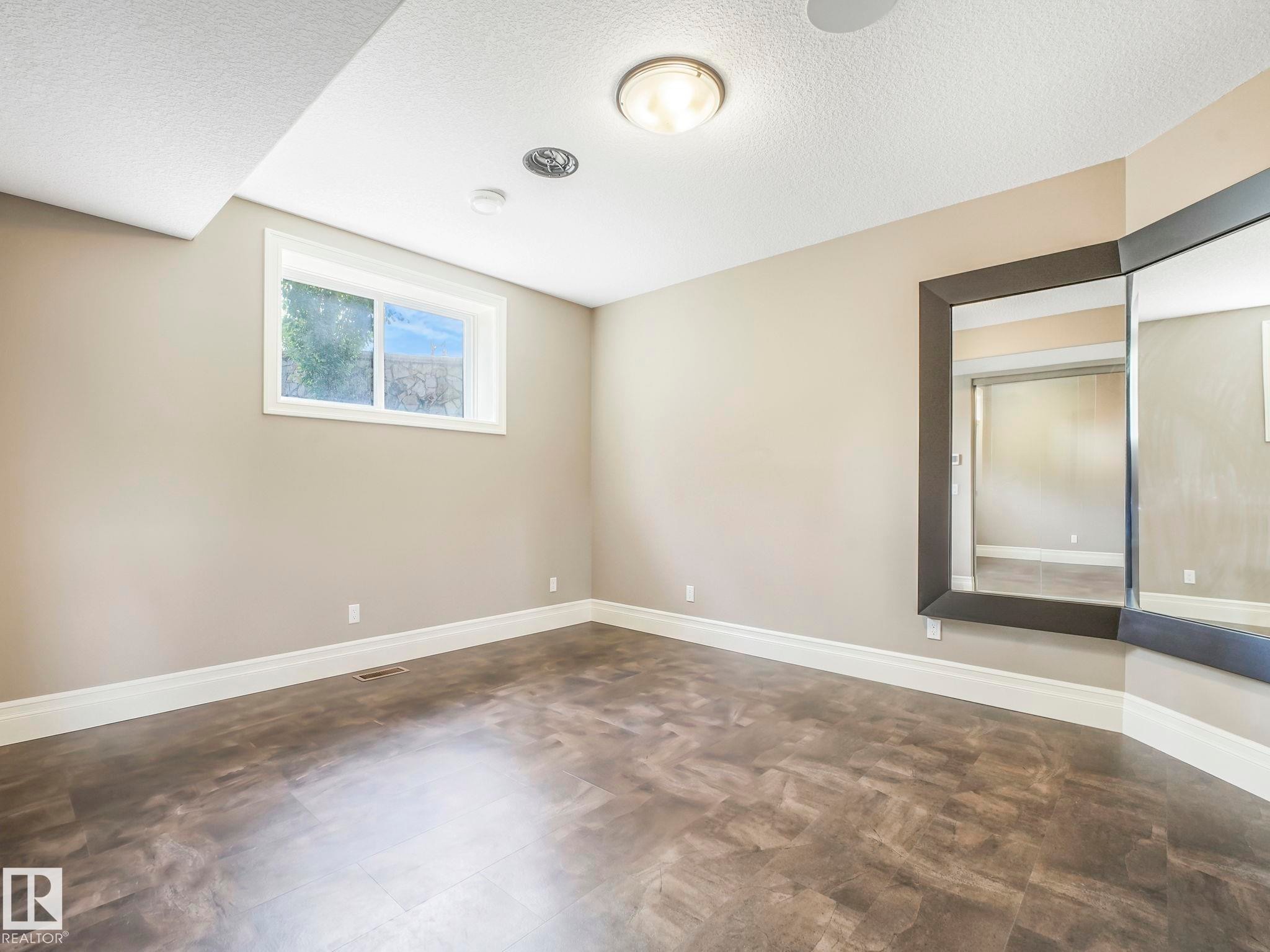 Spacious room featuring wood-finish flooring, a large window, neutral wall paint, and a built-in corner mirror - 2807 Wheaton Drive, Edmonton, AB