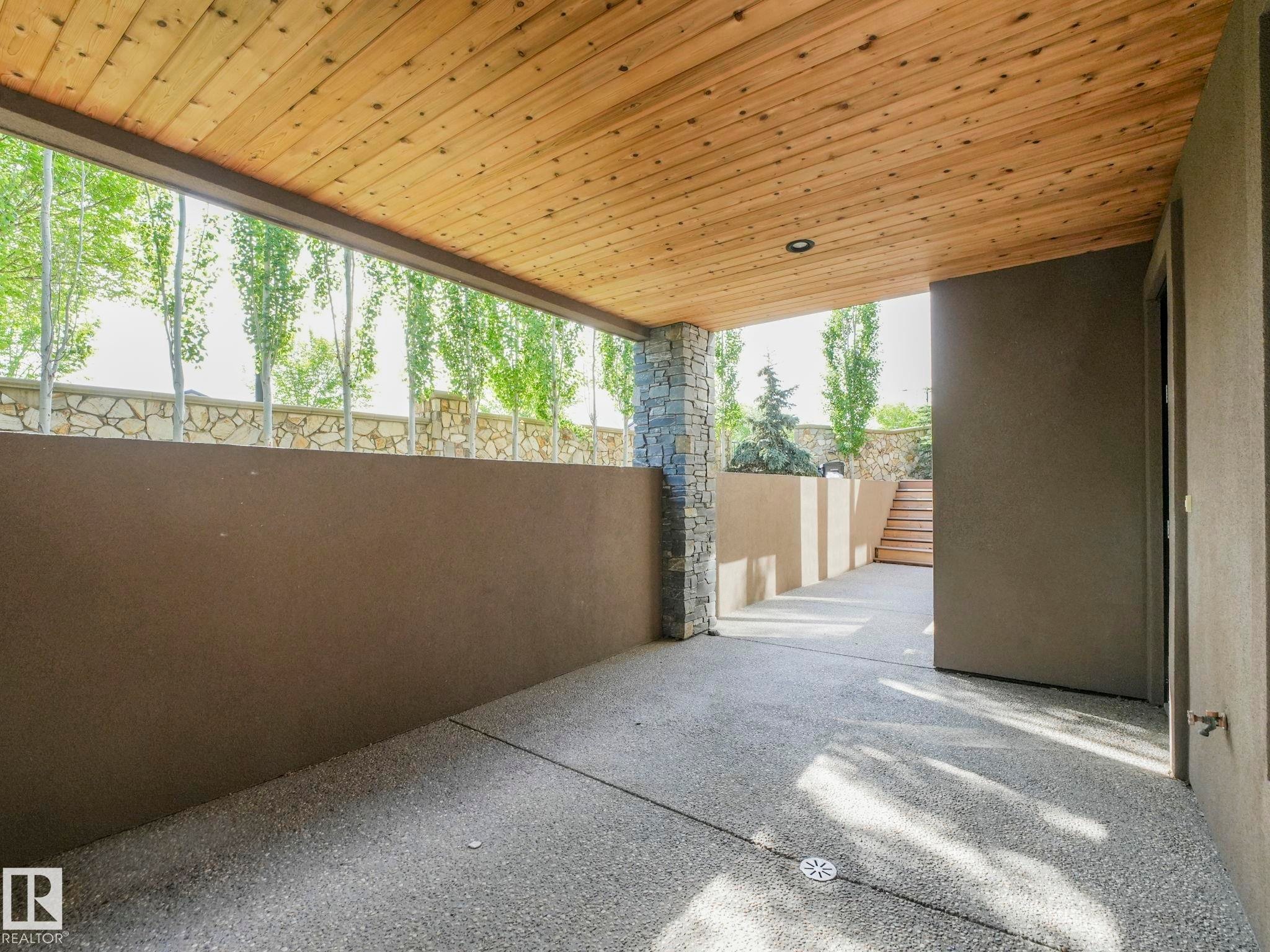 Covered patio featuring a wood-plank ceiling with recessed lighting, exposed aggregate flooring, and a stacked stone column - 2807 Wheaton Drive, Edmonton, AB