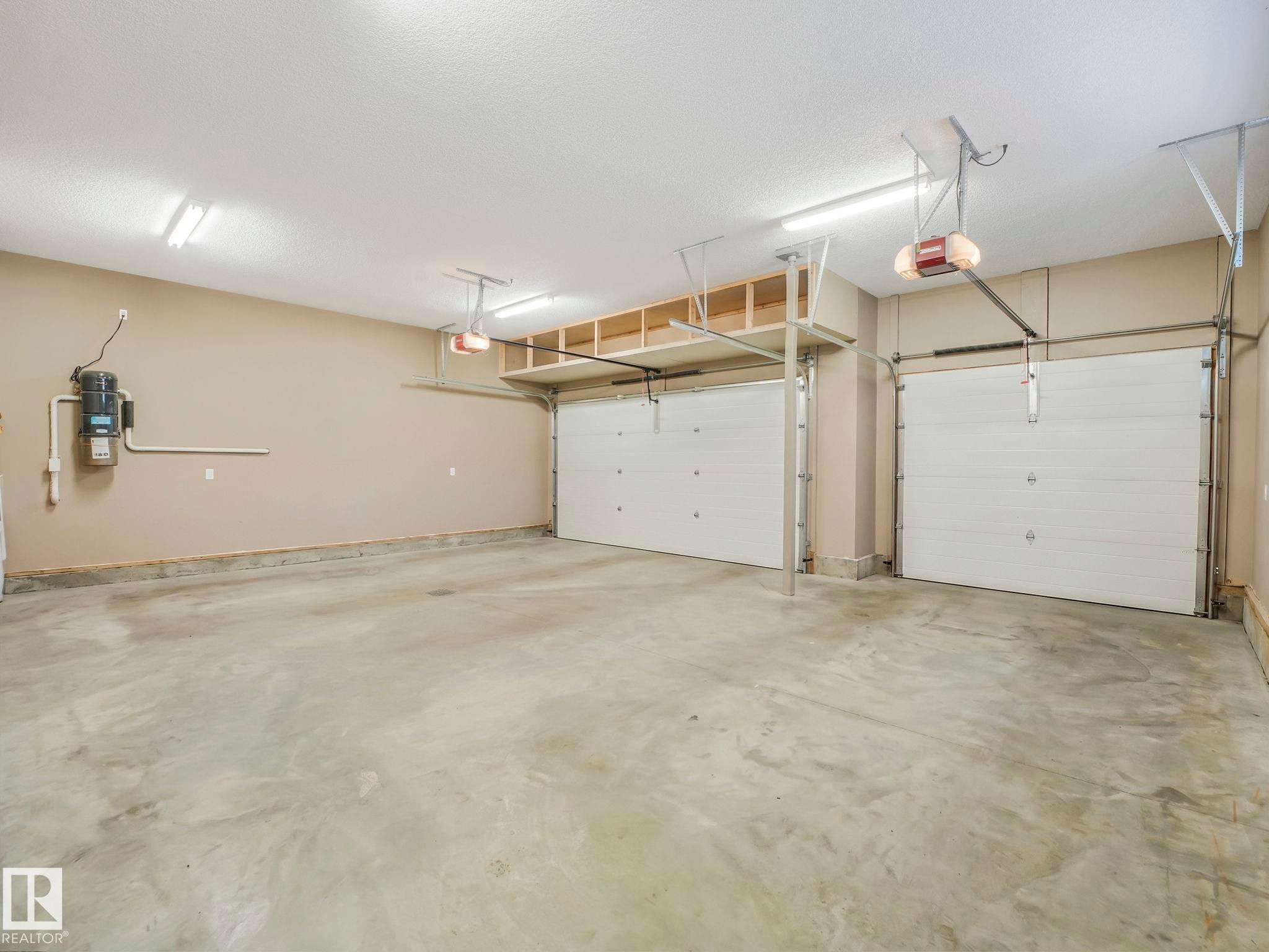 Spacious garage featuring two overhead doors with automatic openers, overhead storage shelving, fluorescent lighting fixtures, and a central vacuum system - 2807 Wheaton Drive, Edmonton, AB