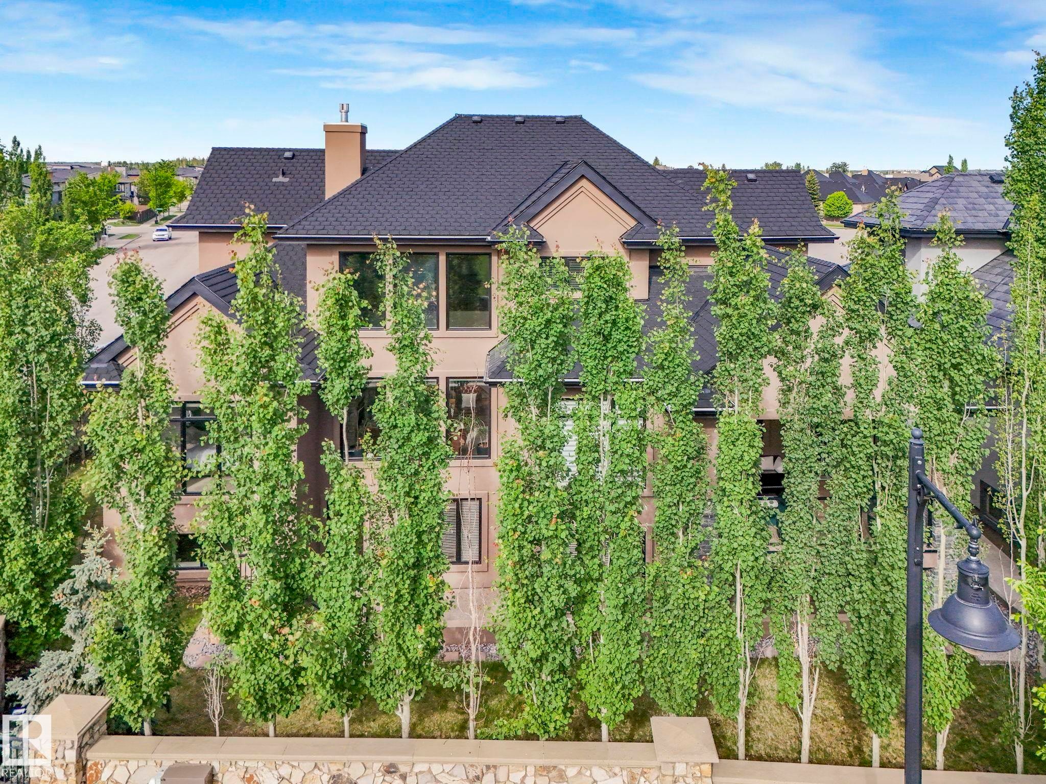 Multi-level property with a dark shingled roof, stucco exterior, and numerous tall, slender trees providing natural screening - 2807 Wheaton Drive, Edmonton, AB