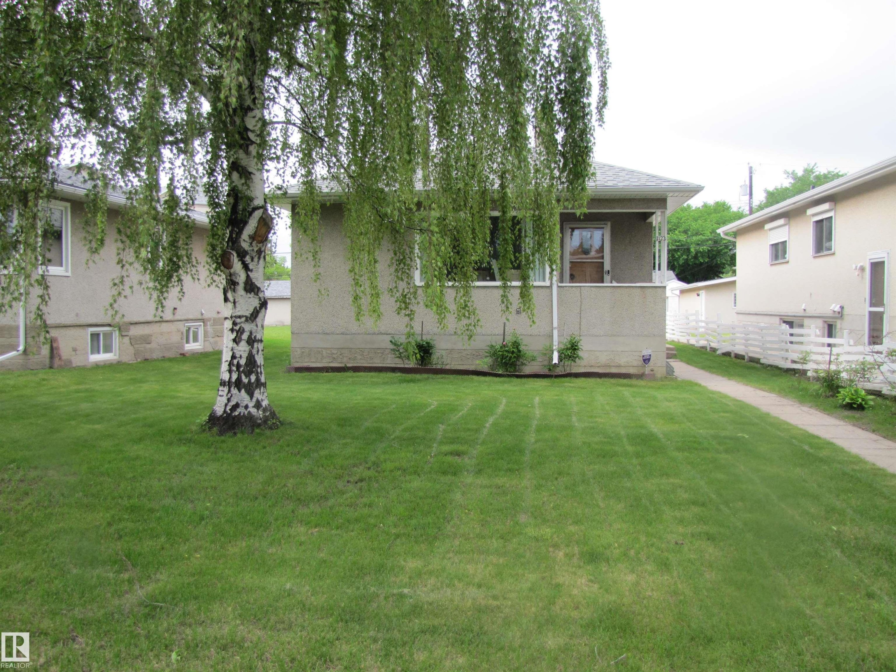 Stucco exterior with a covered front porch, an established front lawn, a mature birch tree, and a concrete walkway - 8122 83 Avenue, Edmonton, AB