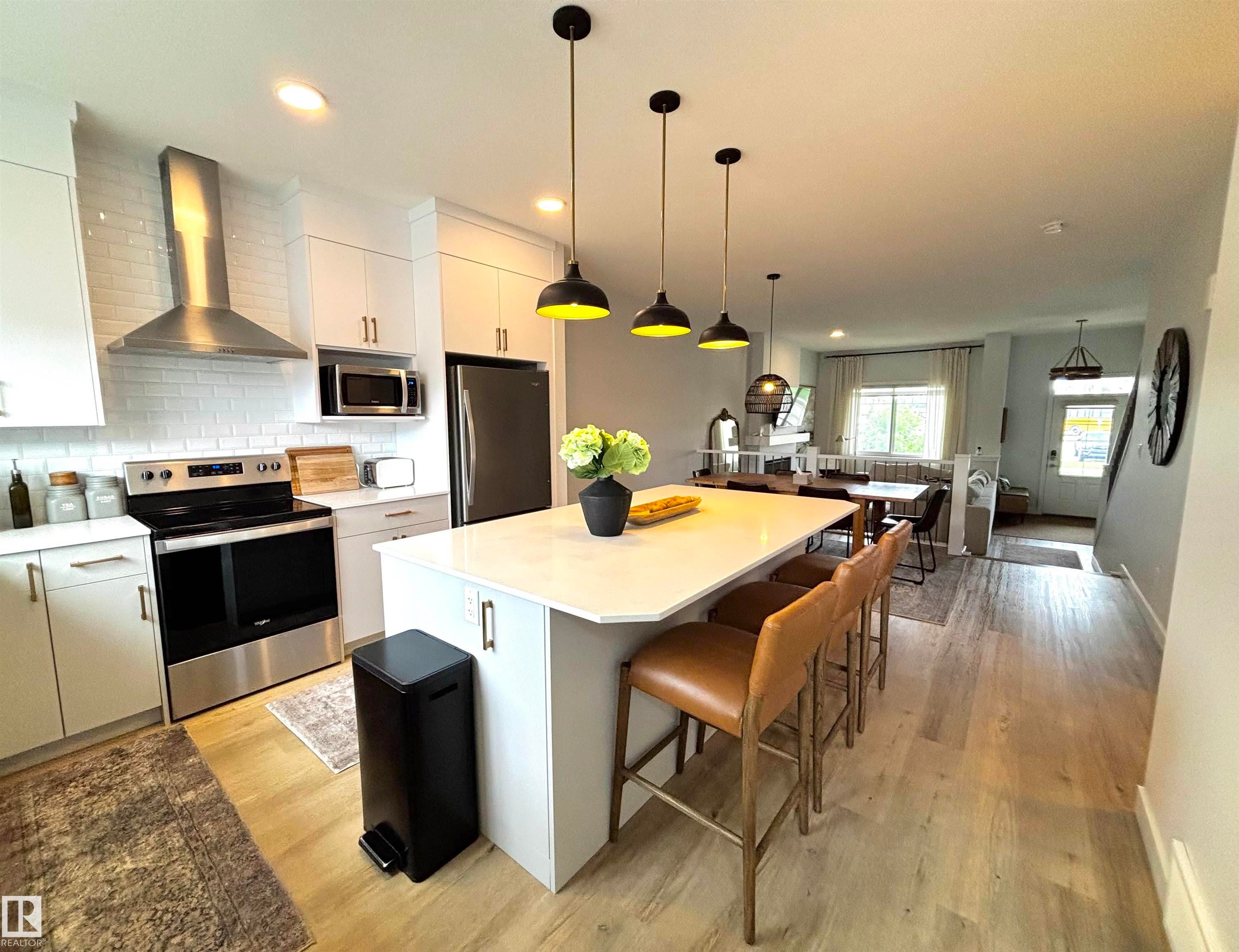Open-concept kitchen featuring an island with seating, white shaker cabinetry, stainless steel appliances, and wood-finish flooring - 5281 Edgemont Boulevard, Edmonton, AB