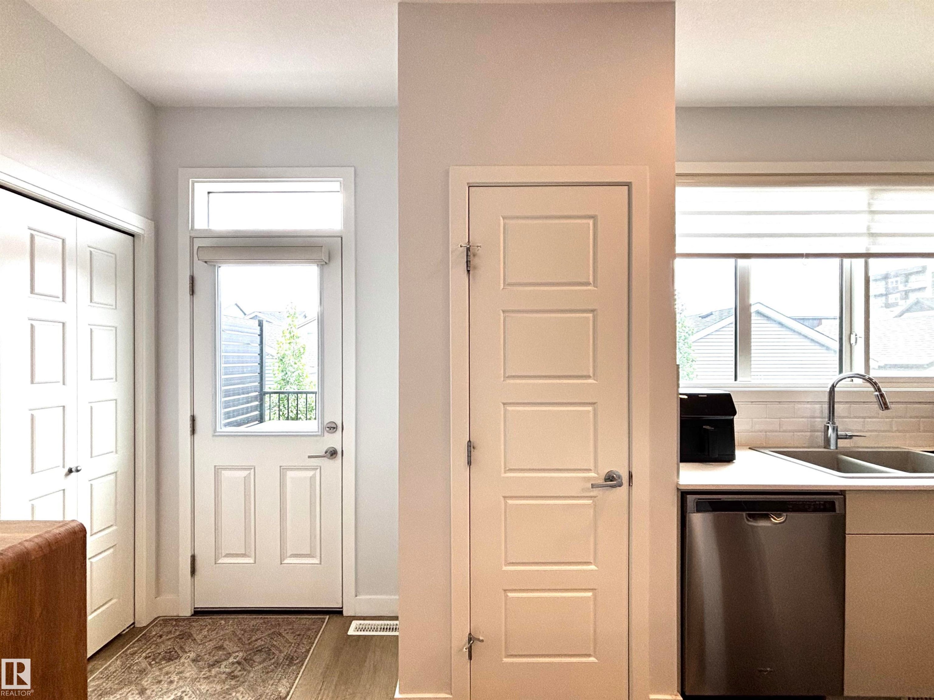 Entrance area with wood-finish flooring, a white paneled door with an overhead transom window, and a built-in closet with bi-fold doors - 5281 Edgemont Boulevard, Edmonton, AB