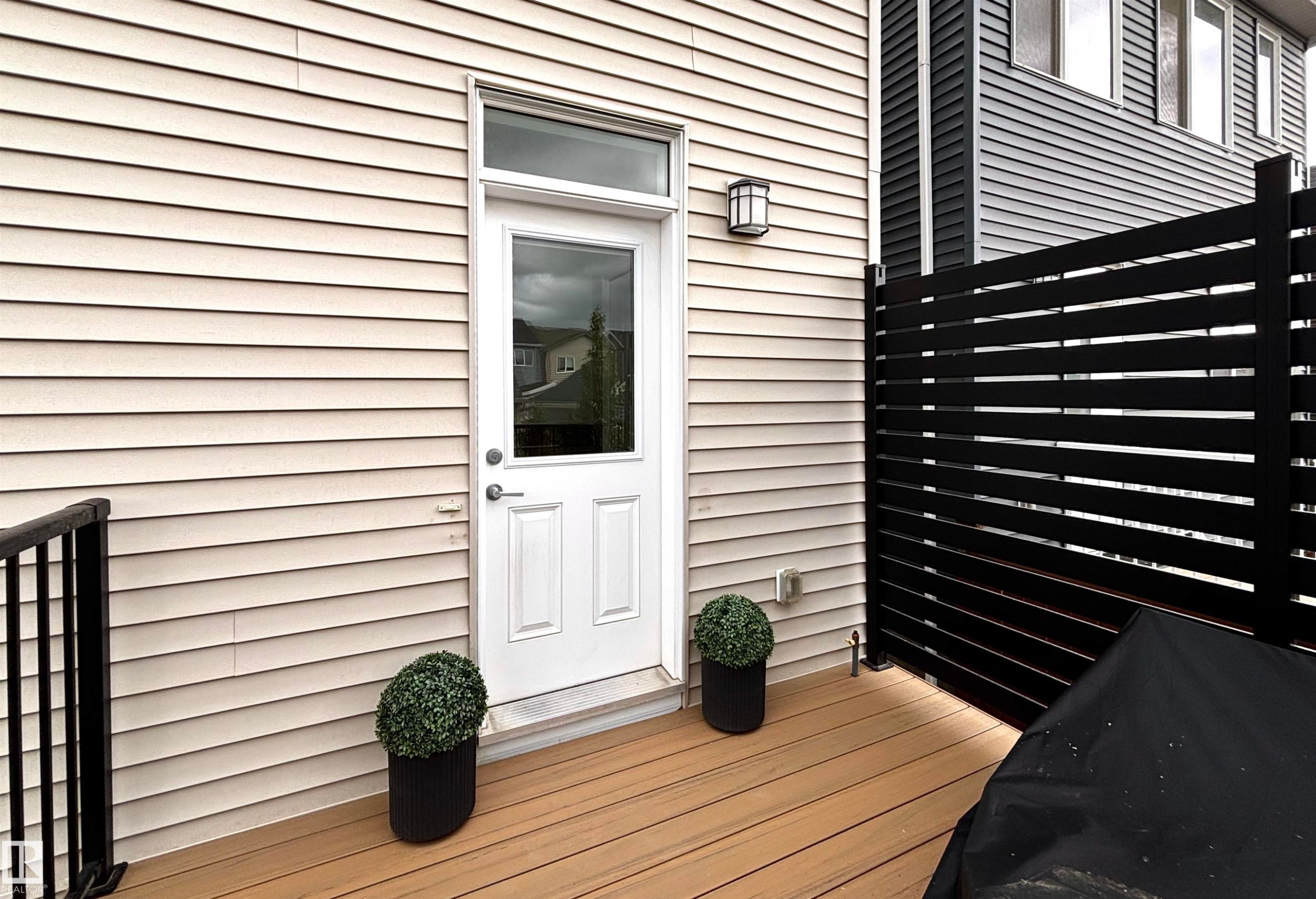 Exterior patio featuring wood-finish decking, horizontal slat privacy fencing, and a modern wall sconce - 5281 Edgemont Boulevard, Edmonton, AB