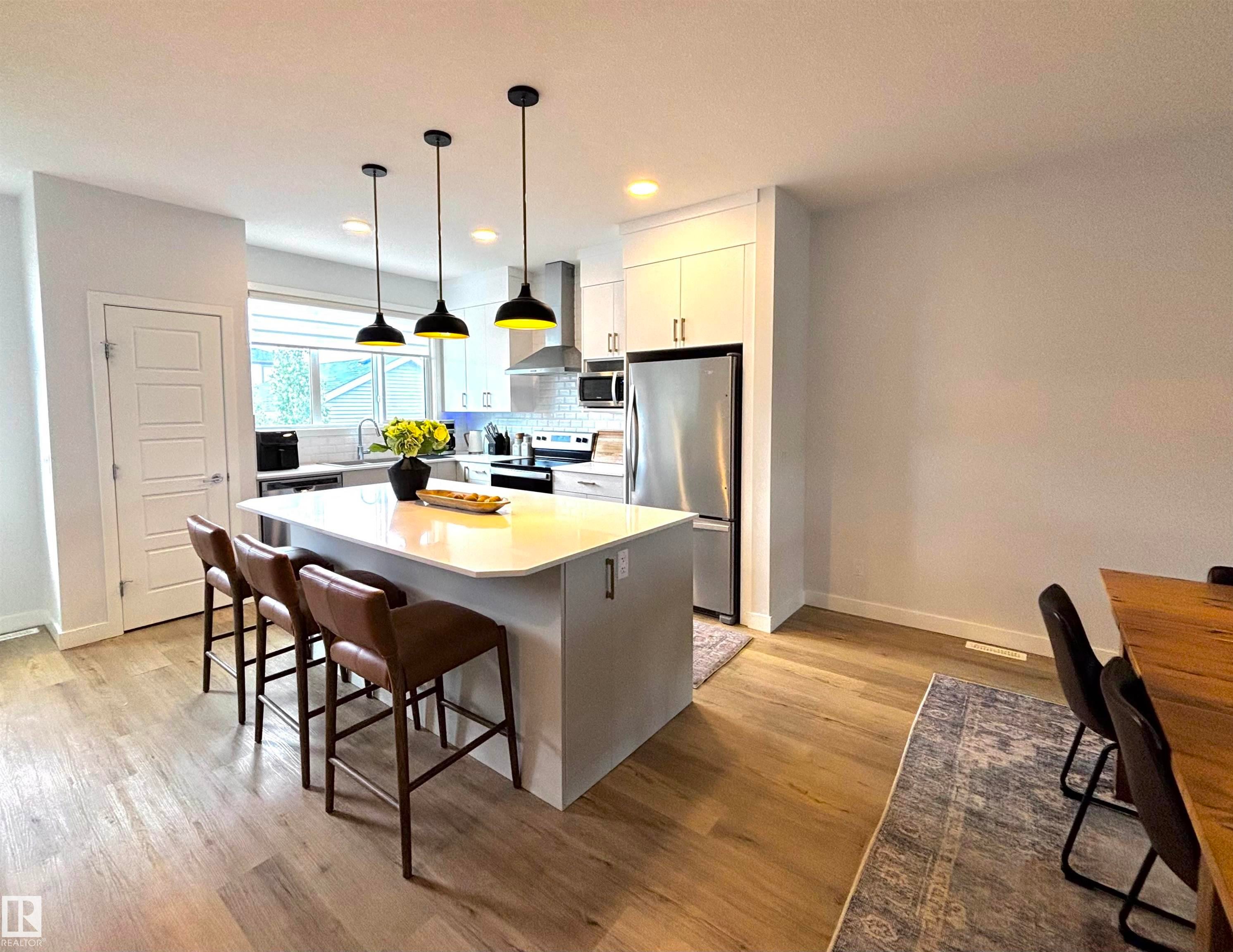Contemporary kitchen featuring a large island with seating, stainless steel appliances, white cabinetry, and light wood-finish flooring - 5281 Edgemont Boulevard, Edmonton, AB