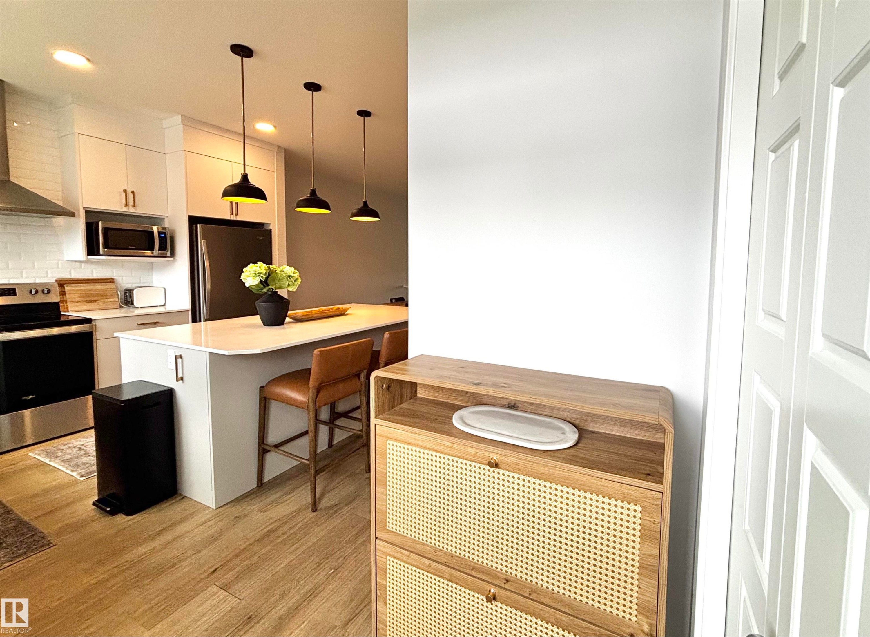 Kitchen featuring white shaker-style cabinetry, stainless steel appliances, a subway tile backsplash, a central island with countertop seating, and wood-finish flooring - 5281 Edgemont Boulevard, Edmonton, AB
