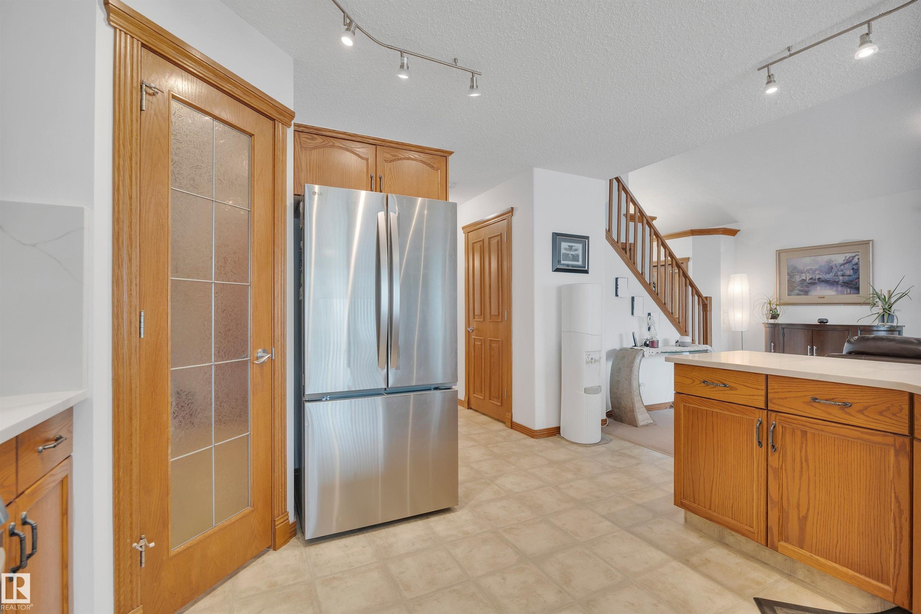 Kitchen area featuring a stainless steel French door refrigerator, wood-finish cabinetry, and light-toned tile flooring - 16512 87 Street Nw, Edmonton, AB - Indoor