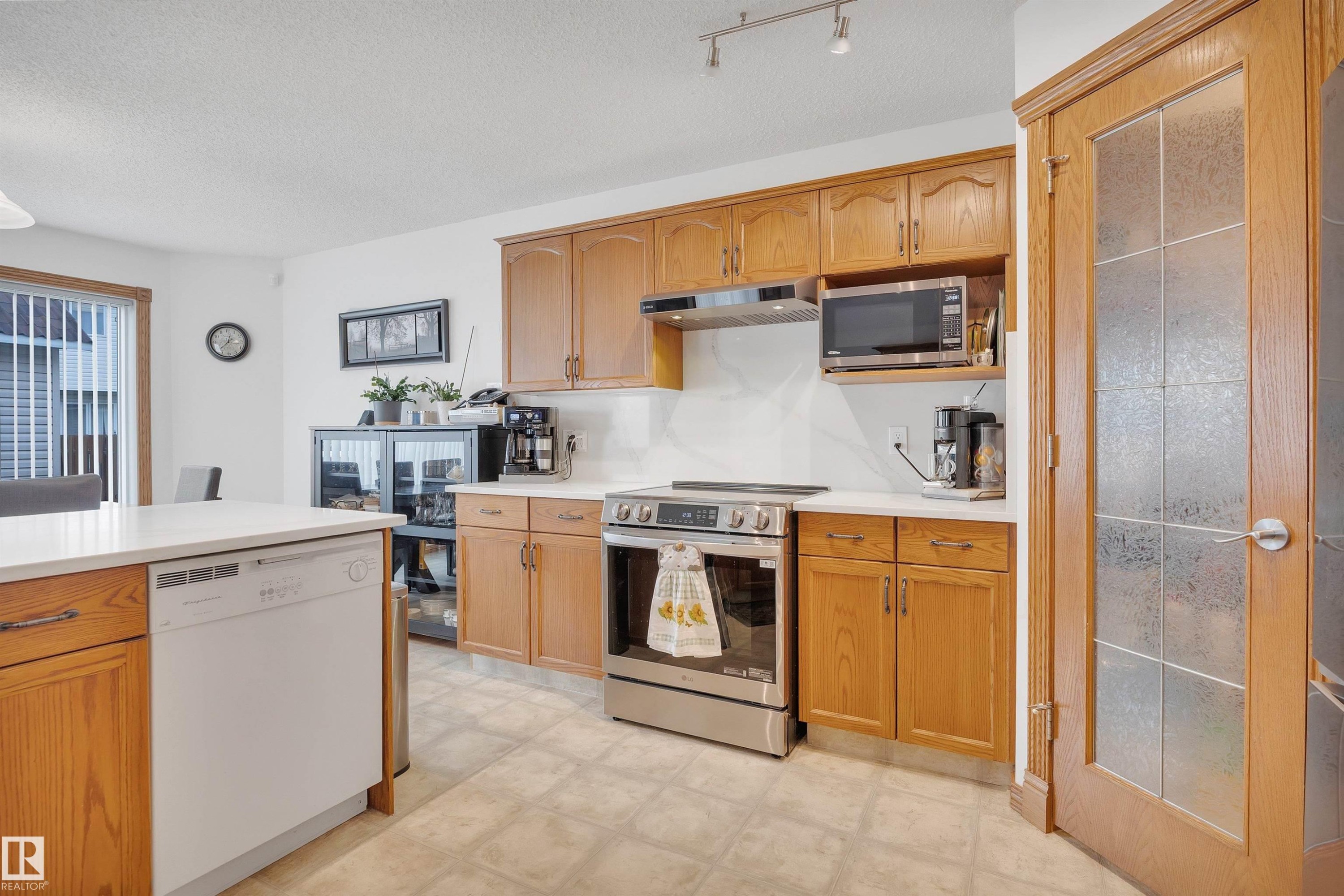 Kitchen featuring wood cabinetry, light-toned countertops, tile flooring, and stainless steel appliances - 16512 87 Street Nw, Edmonton, AB - Indoor Photo Showing Kitchen