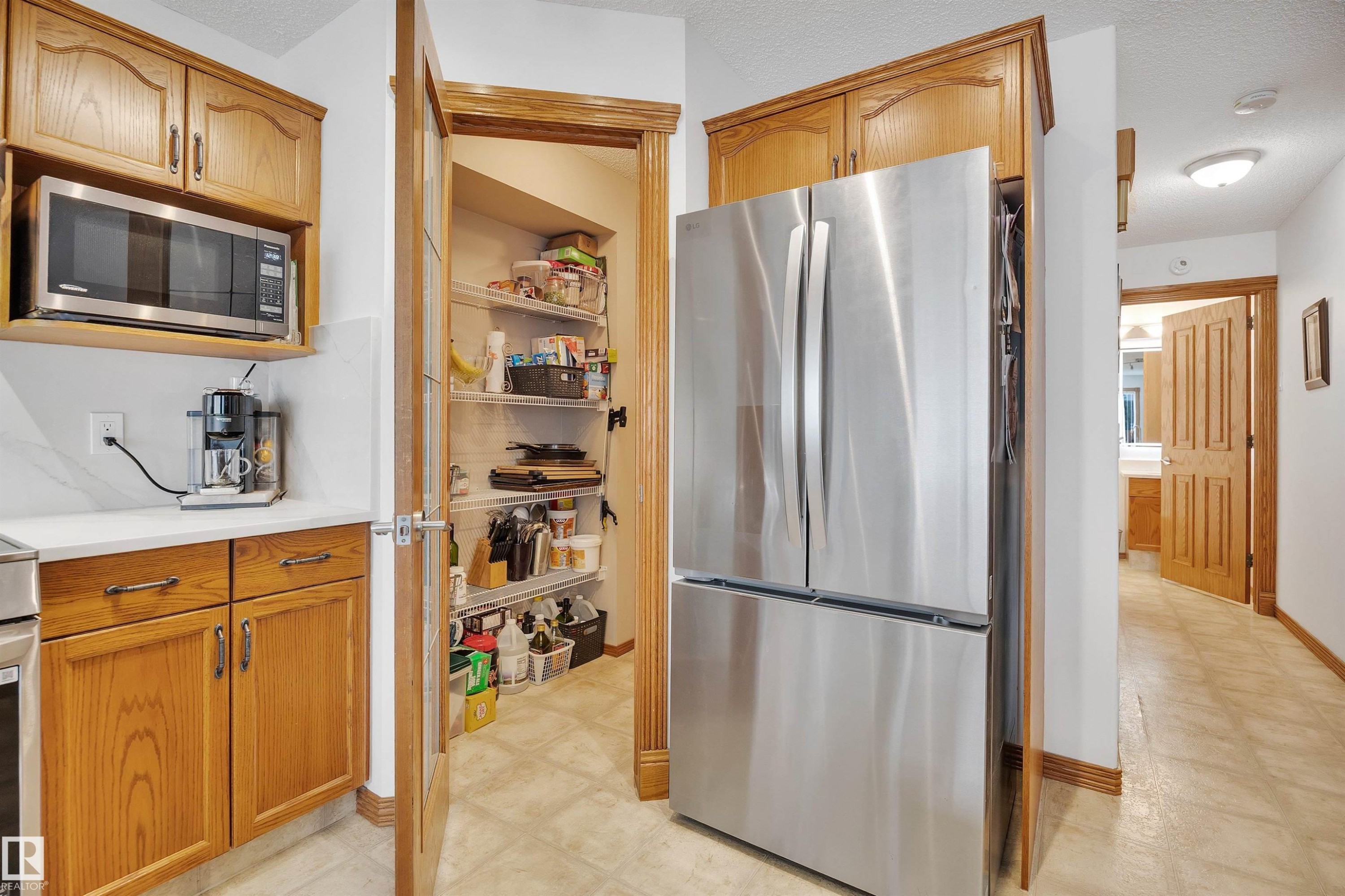 Kitchen area featuring a stainless steel French door refrigerator, built-in microwave, white countertops, and wood-finish cabinetry - 16512 87 Street Nw, Edmonton, AB - Indoor Photo Showing Kitchen