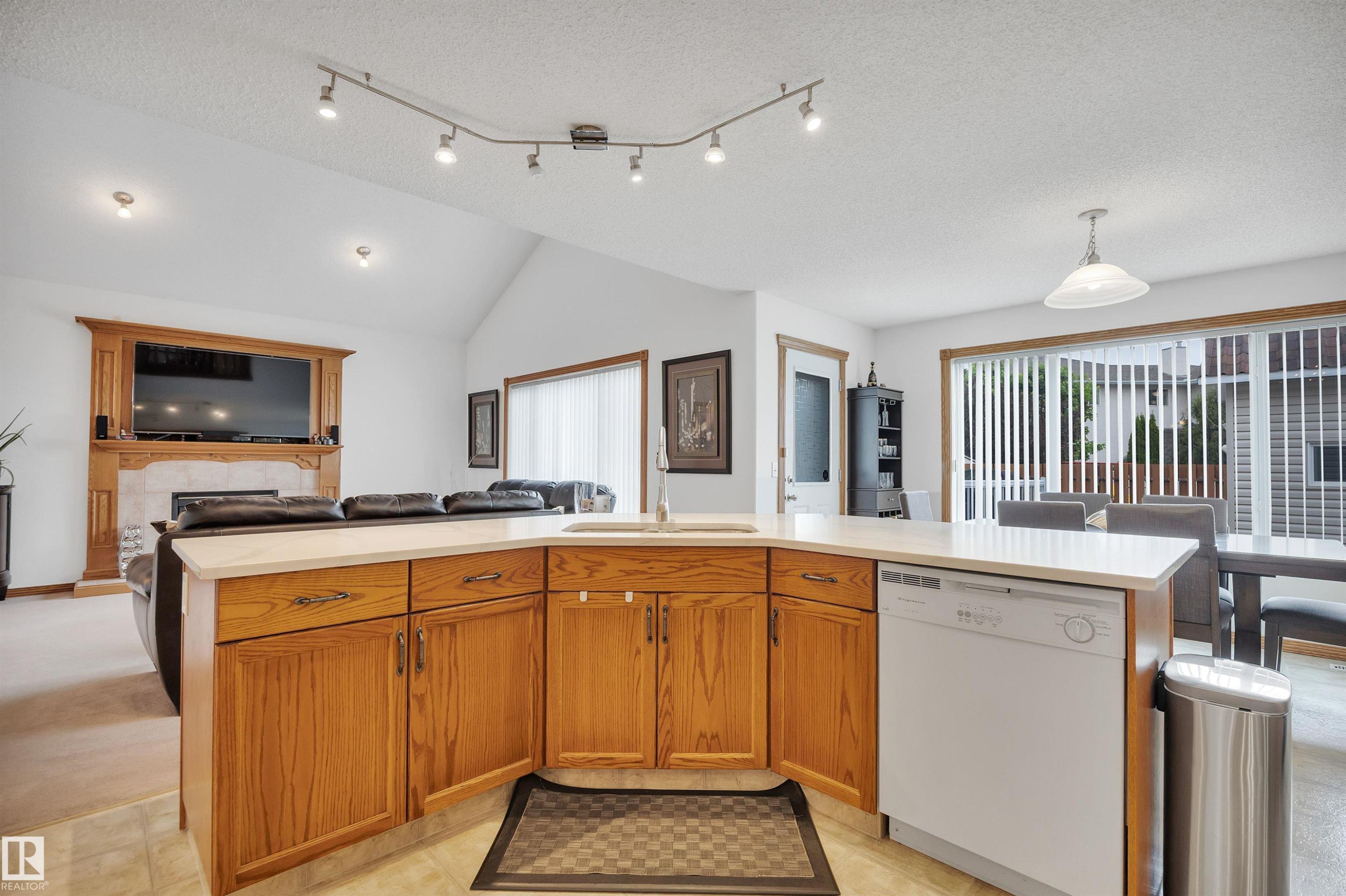 Open-concept kitchen featuring wood cabinetry, a built-in sink, and a dishwasher, with a vaulted ceiling and track lighting - 16512 87 Street Nw, Edmonton, AB - Indoor Photo Showing Kitchen With Double Sink