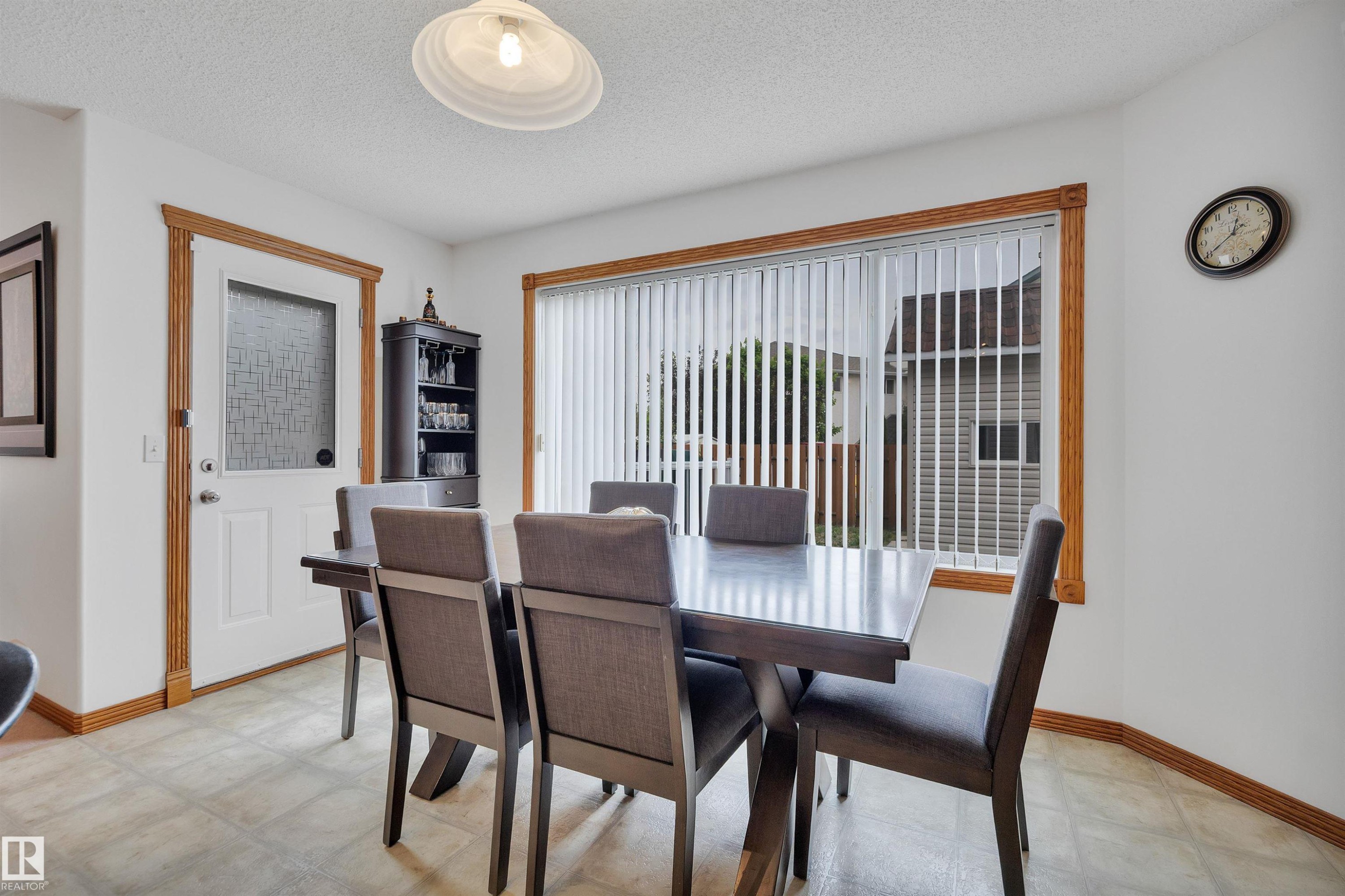 Dining area featuring a large window with vertical blinds, a white paneled door with frosted glass, wood-finish trim, and neutral-toned flooring - 16512 87 Street Nw, Edmonton, AB - Indoor Photo Showing Dining Room