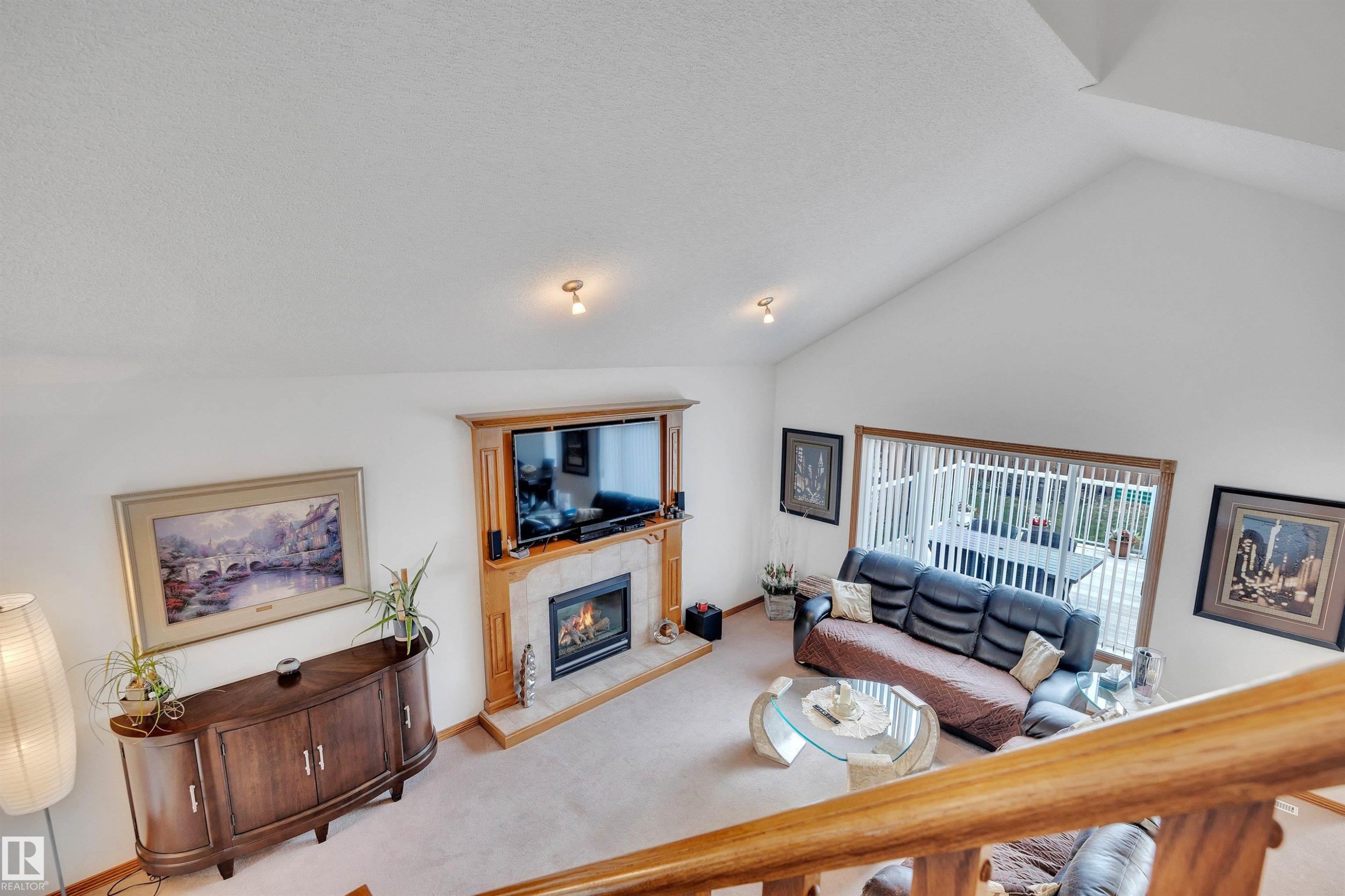 Vaulted ceiling living space featuring a wood-surround fireplace with a tiled hearth, an expansive window with vertical blinds, and neutral carpeting - 16512 87 Street Nw, Edmonton, AB - Indoor Photo Showing Living Room With Fireplace
