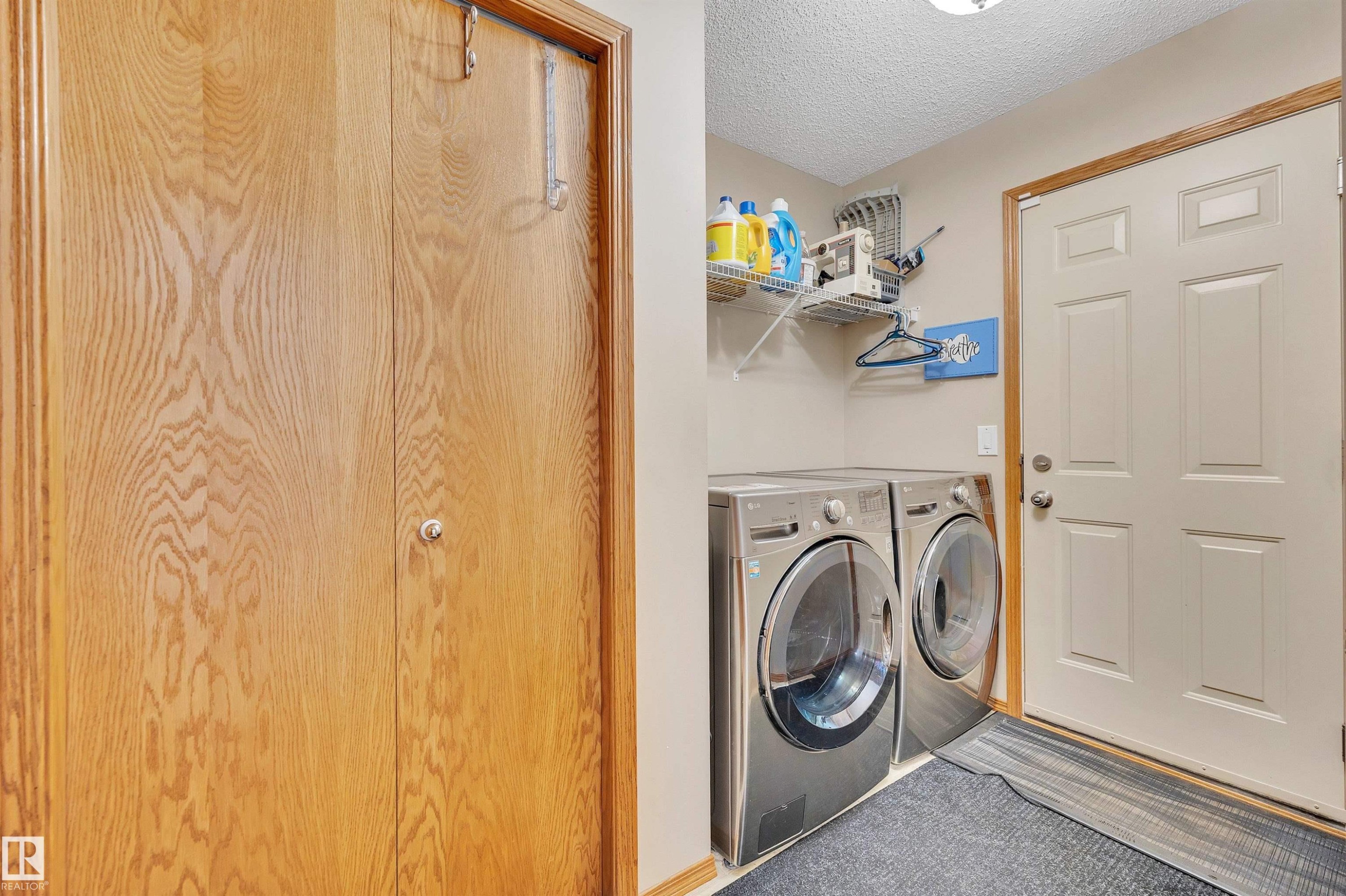 Dedicated laundry area featuring front-loading machines, wall-mounted shelving, and a paneled entry door - 16512 87 Street Nw, Edmonton, AB - Indoor Photo Showing Laundry Room
