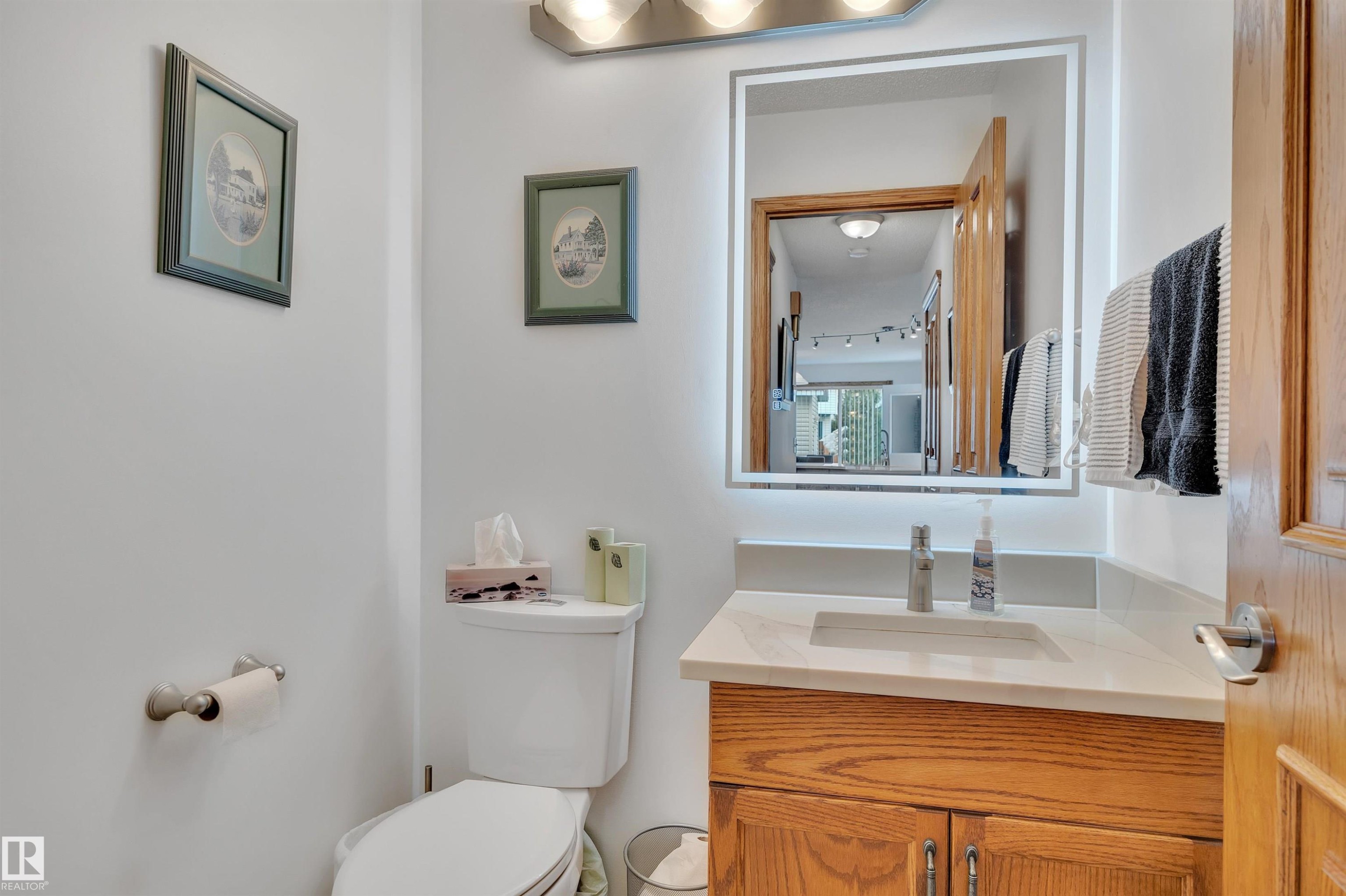 Bathroom featuring a wood vanity with a light-colored countertop, an integrated sink, and an illuminated mirror - 16512 87 Street Nw, Edmonton, AB - Indoor Photo Showing Bathroom