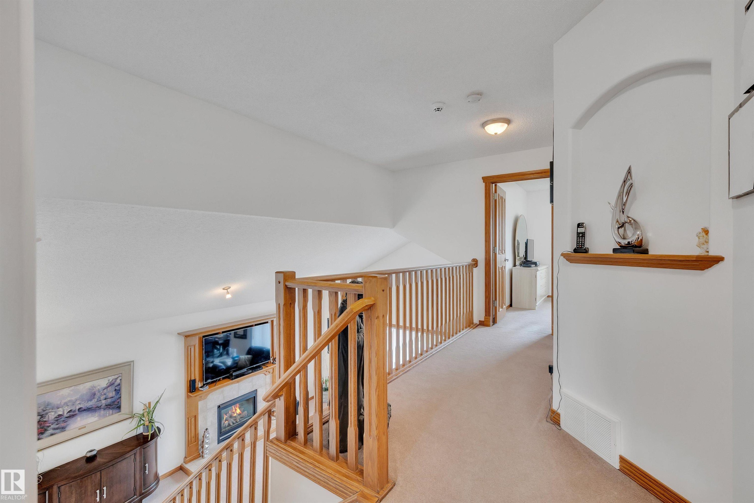 Second-floor hallway featuring a wood-finish railing, neutral carpet, and an arched wall niche with a wood-finish shelf - 16512 87 Street Nw, Edmonton, AB - Indoor Photo Showing Other Room