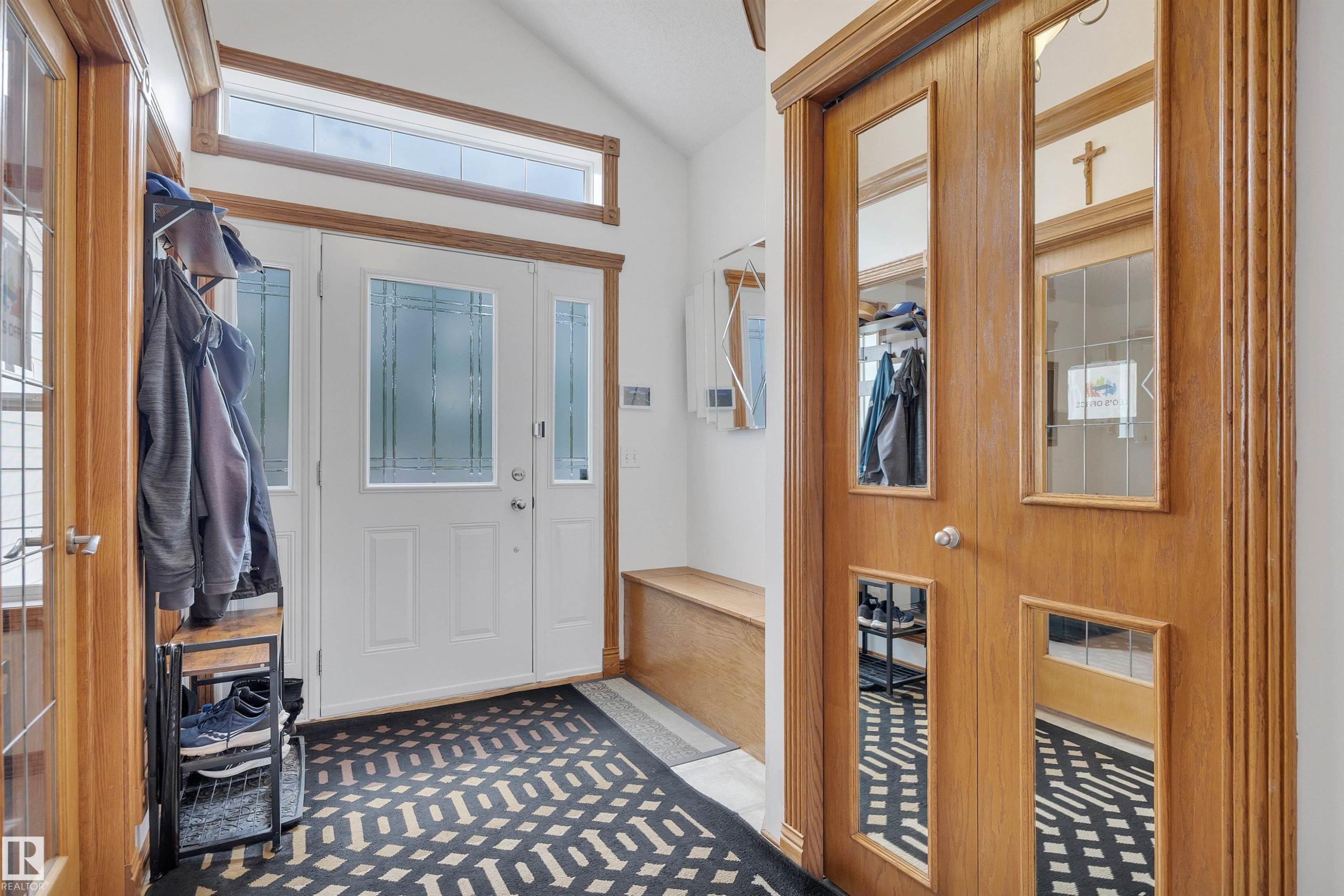 White front entry door with decorative glass inserts and transom window, complemented by a built-in wooden bench and wood-finish closet doors with mirrored panels - 16512 87 Street Nw, Edmonton, AB - Indoor Photo Showing Other Room