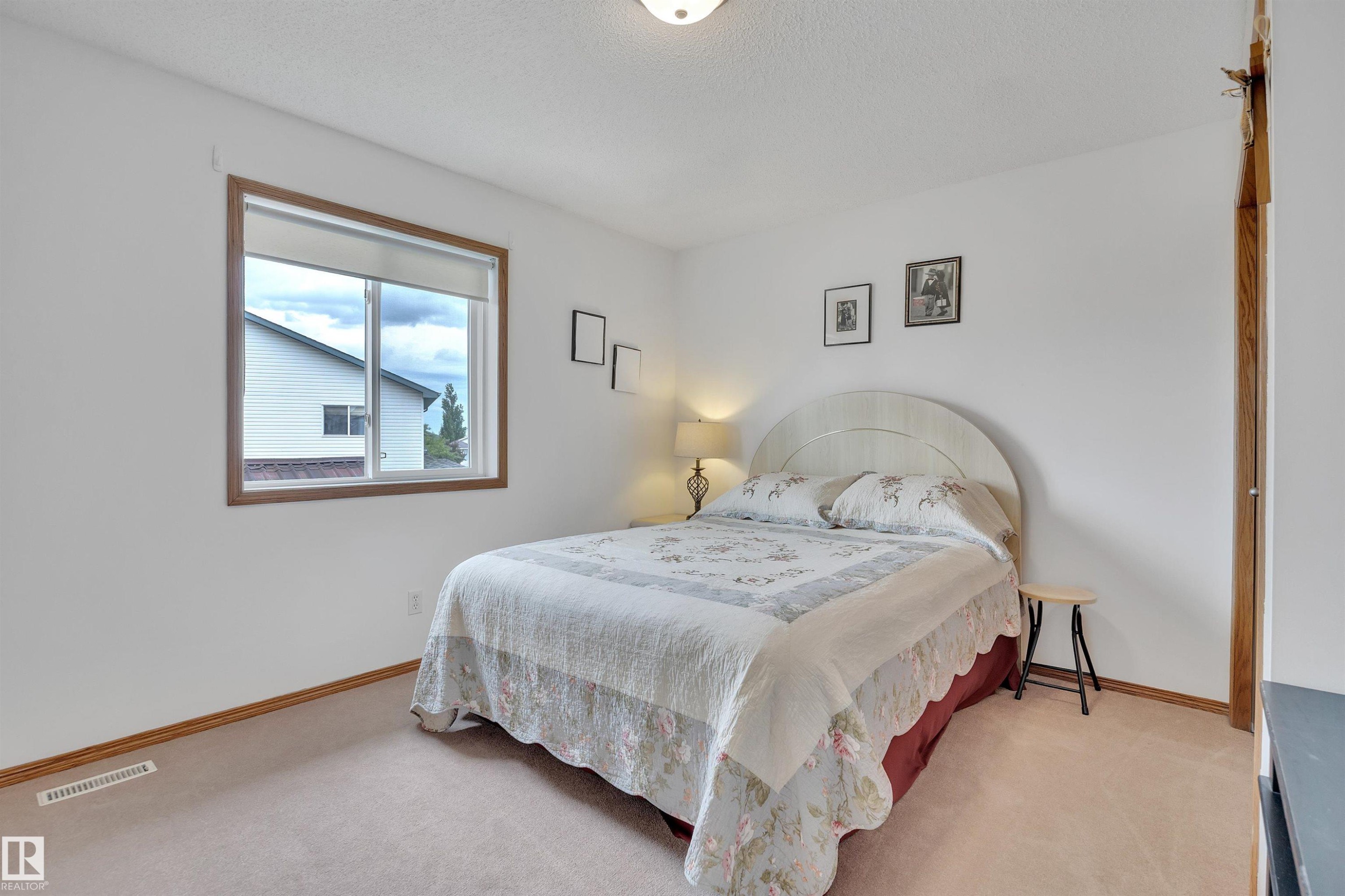 Carpeted bedroom with a single window featuring a wood-finish frame and roller shade - 16512 87 Street Nw, Edmonton, AB - Indoor Photo Showing Bedroom