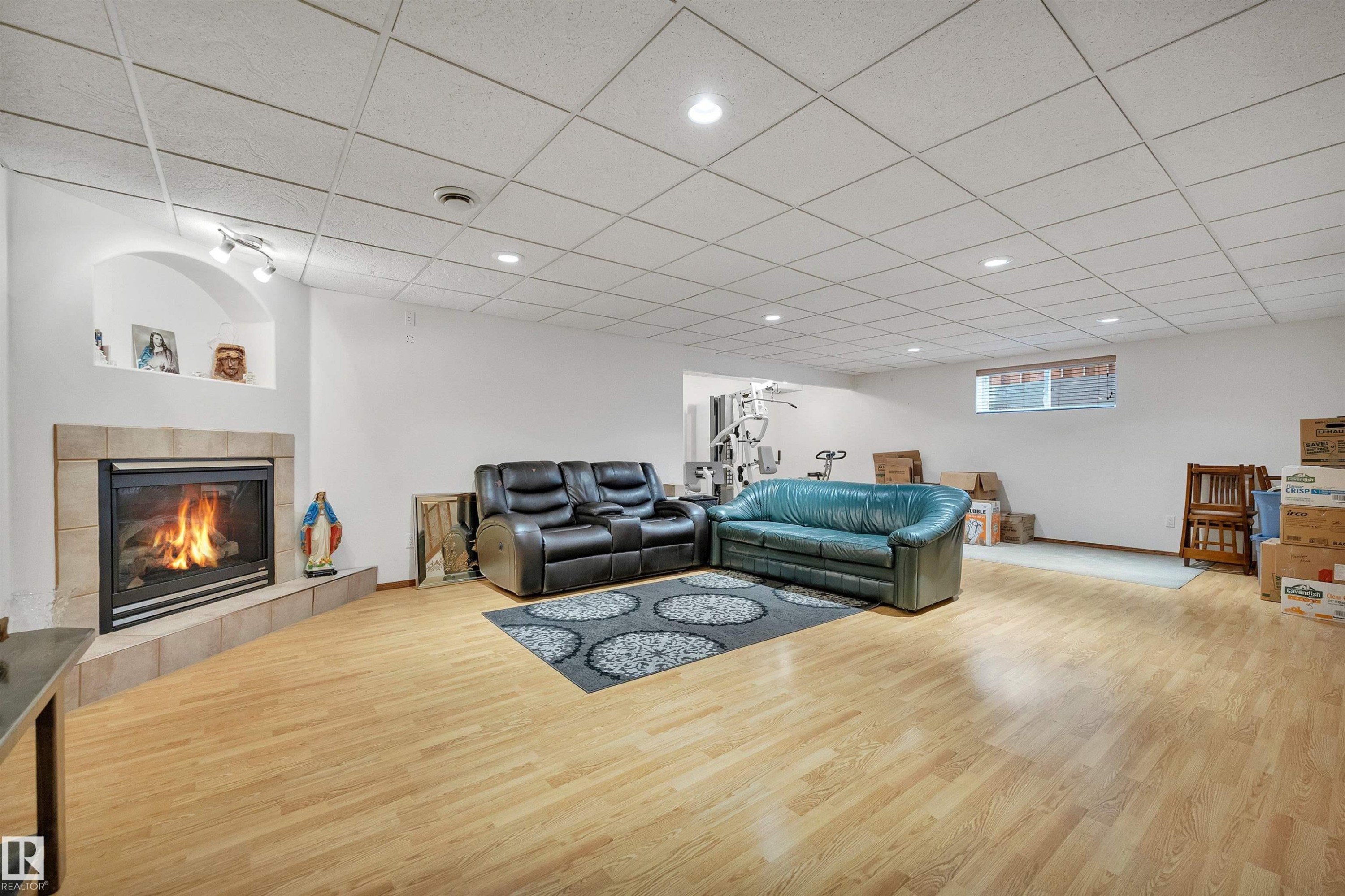 Tiled fireplace with hearth, wood-finish flooring, recessed lighting, drop ceiling, and a large window - 16512 87 Street Nw, Edmonton, AB - Indoor With Fireplace