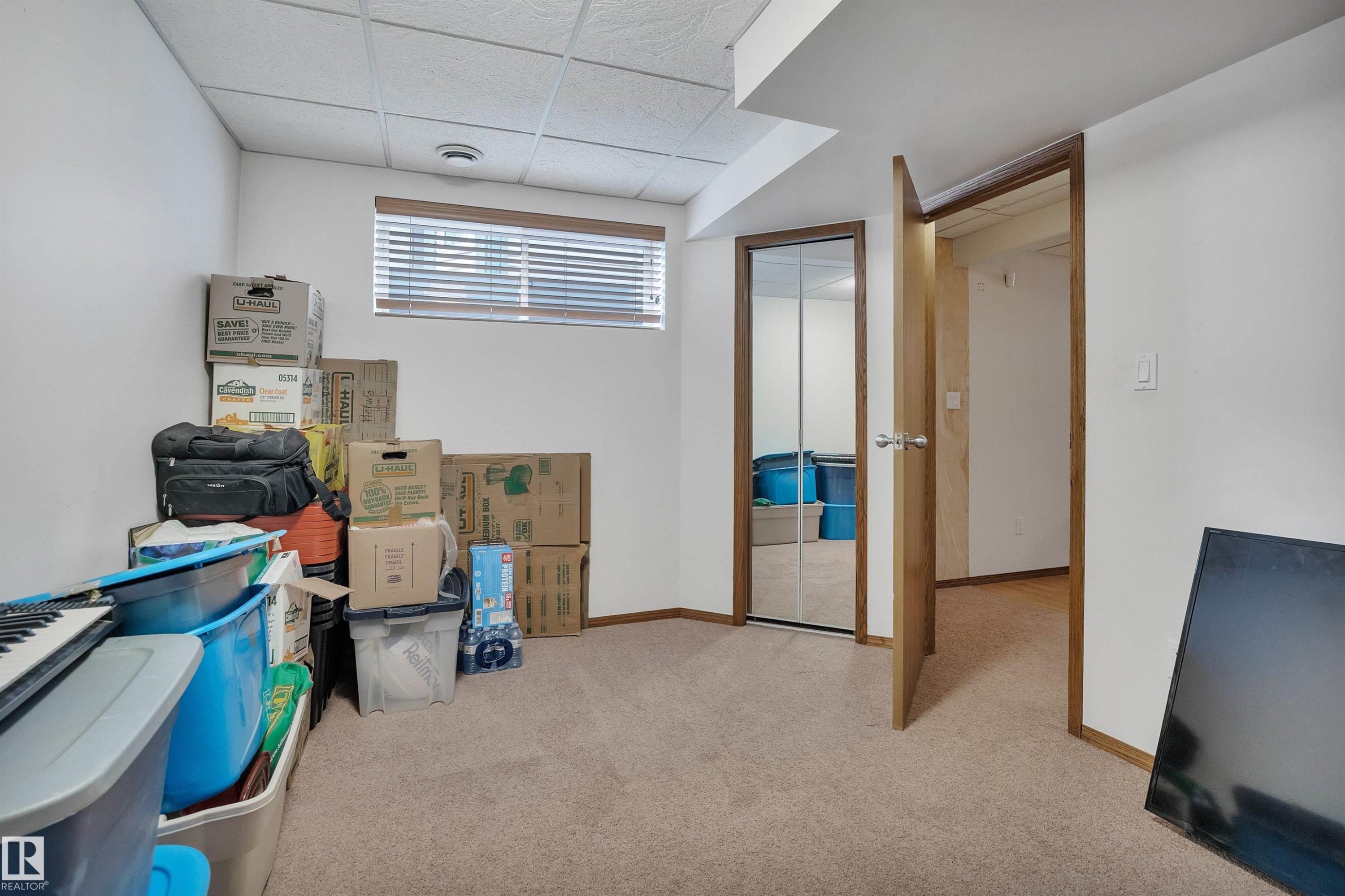 Carpeted room featuring a drop ceiling, a horizontal window with blinds, and a mirrored closet door - 16512 87 Street Nw, Edmonton, AB - Indoor
