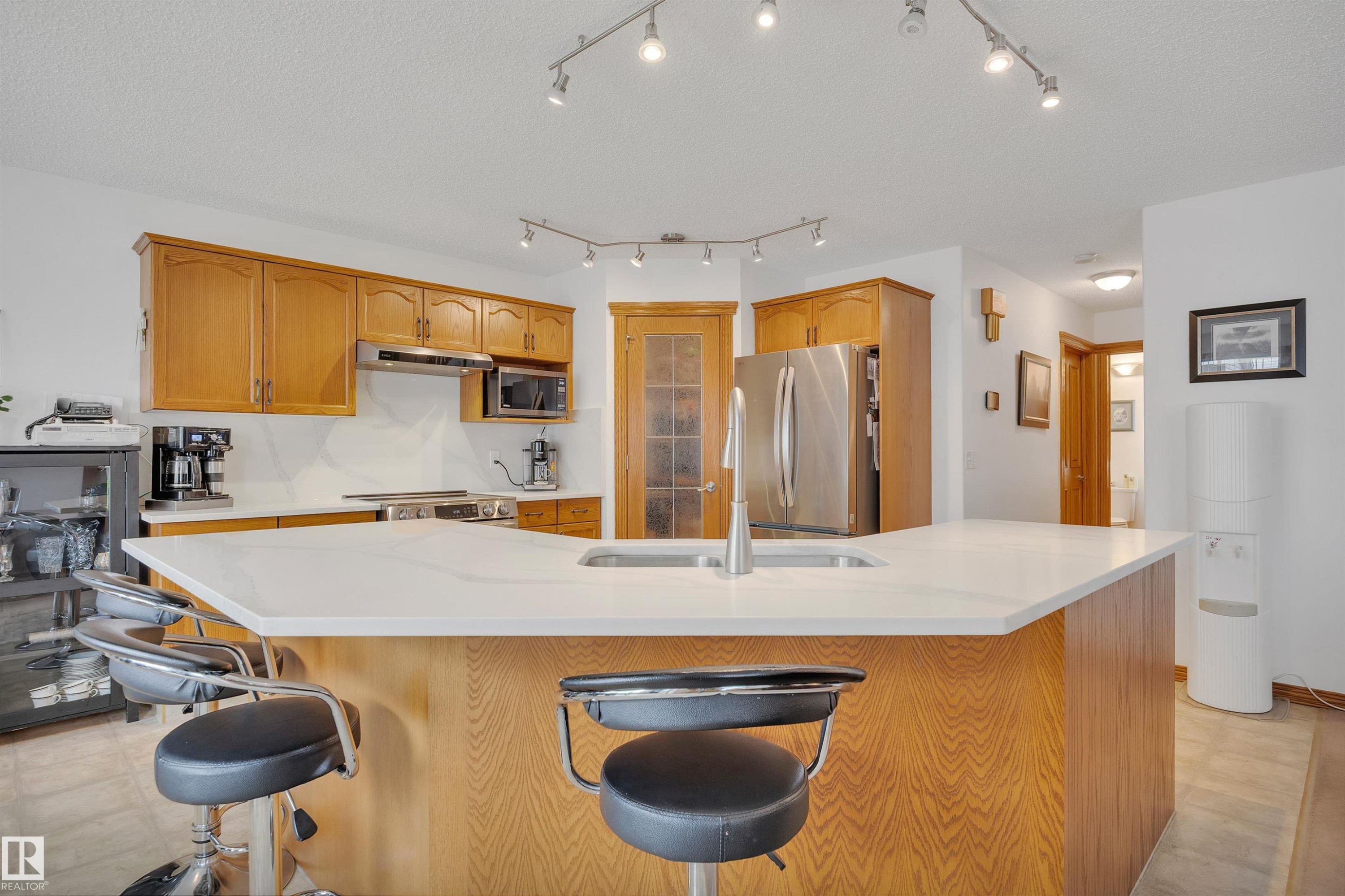 Central kitchen island with a white countertop and integrated sink, complemented by wood-finish cabinetry - 16512 87 Street Nw, Edmonton, AB - Indoor Photo Showing Kitchen With Double Sink